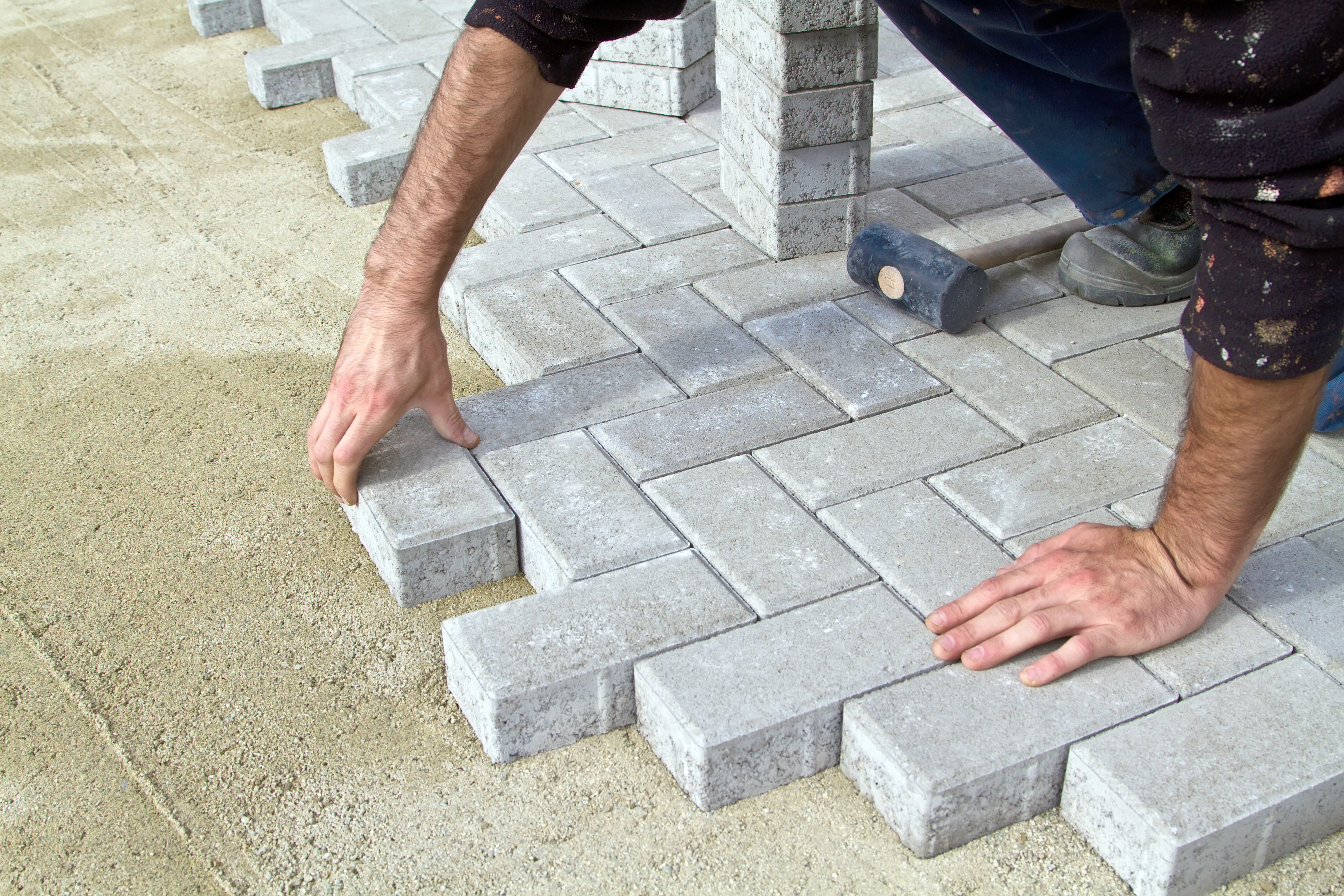 Stratenmaker legt betonklinkers op een zandbed voor de aanleg van een nieuwe bestrating.