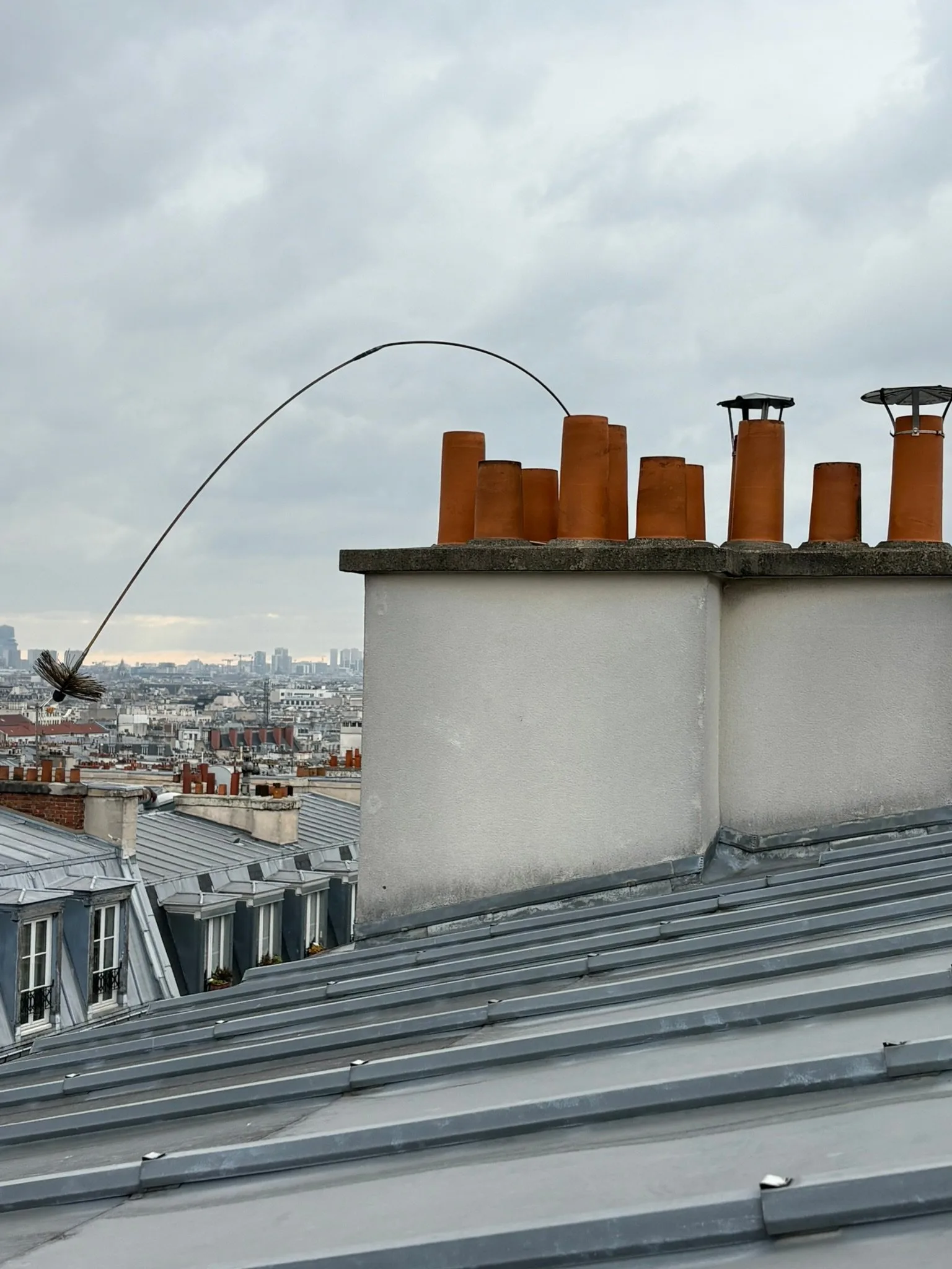 Hérisson de ramonage en action sur une souche de cheminée au-dessus des toits parisiens