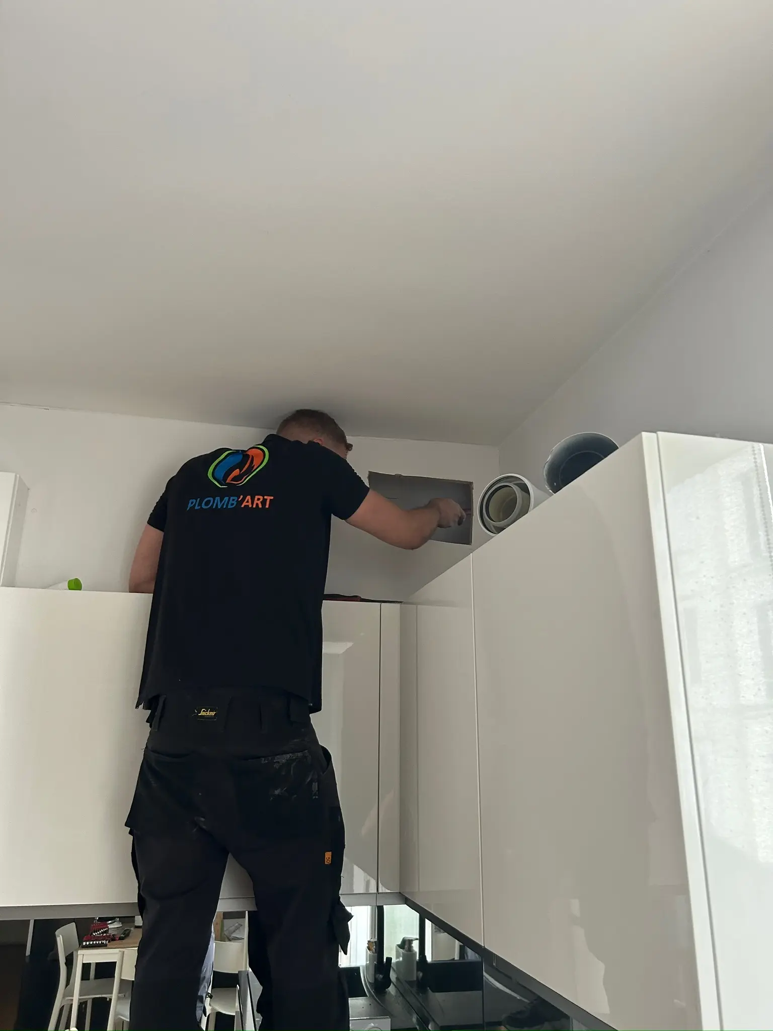 Technicien Plomb'Art posant la plaque d'un conduit de ventilation au-dessus des meubles hauts