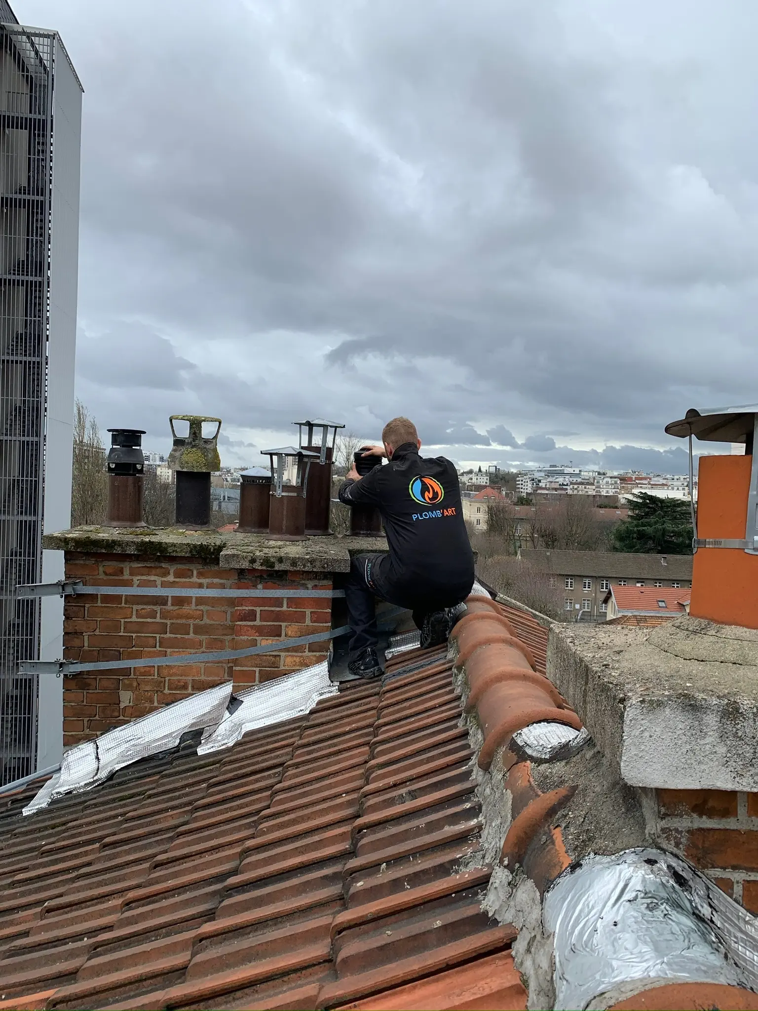 Technicien Plomb'Art intervenant sur les souches de cheminée d'un toit en tuiles à Paris