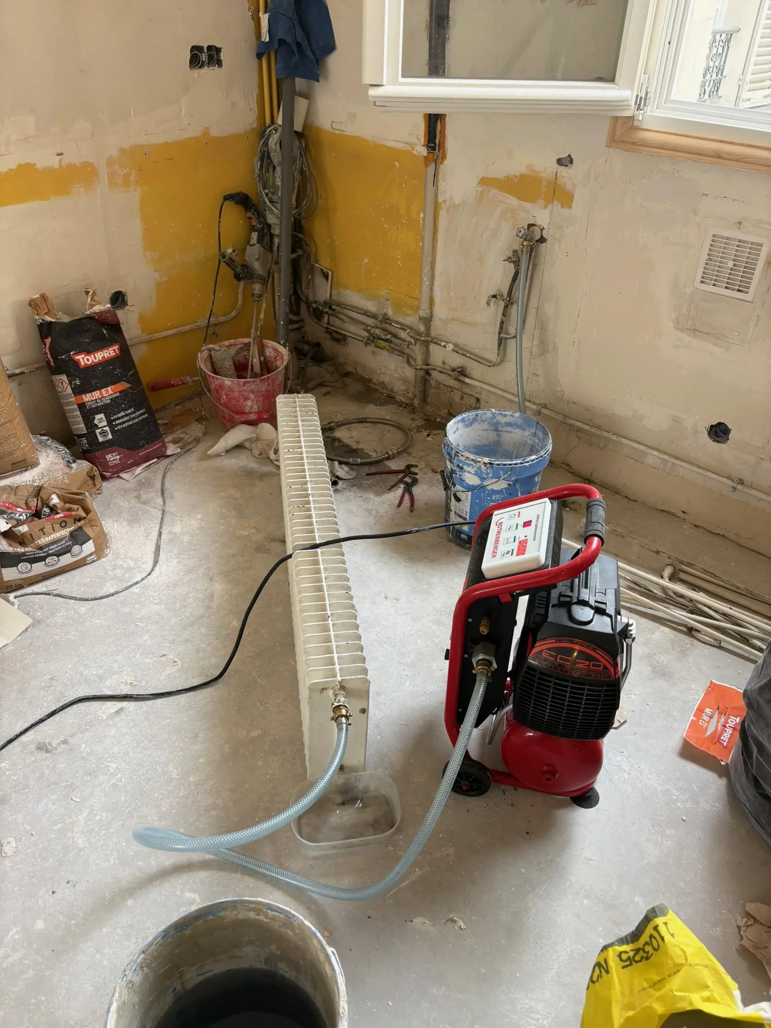 Radiateur déposé et raccordé à une pompe de rinçage sur un chantier de rénovation d'appartement