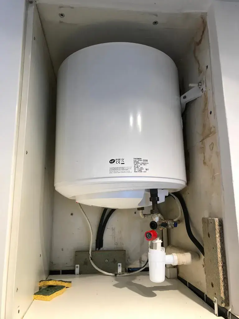 Ballon d'eau chaude installé en placard avec son groupe de sécurité rouge et son siphon d'évacuation