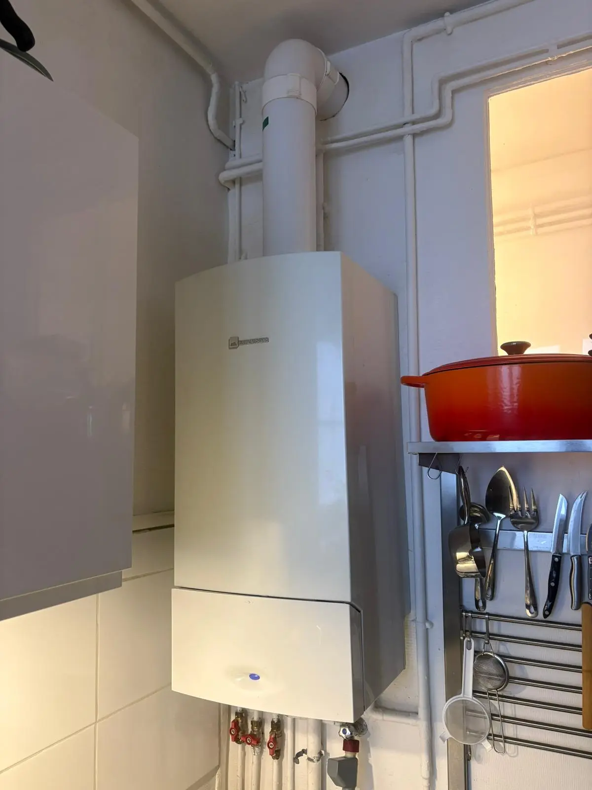 Chaudière gaz murale installée dans un angle de cuisine, conduit d'évacuation et vannes apparentes
