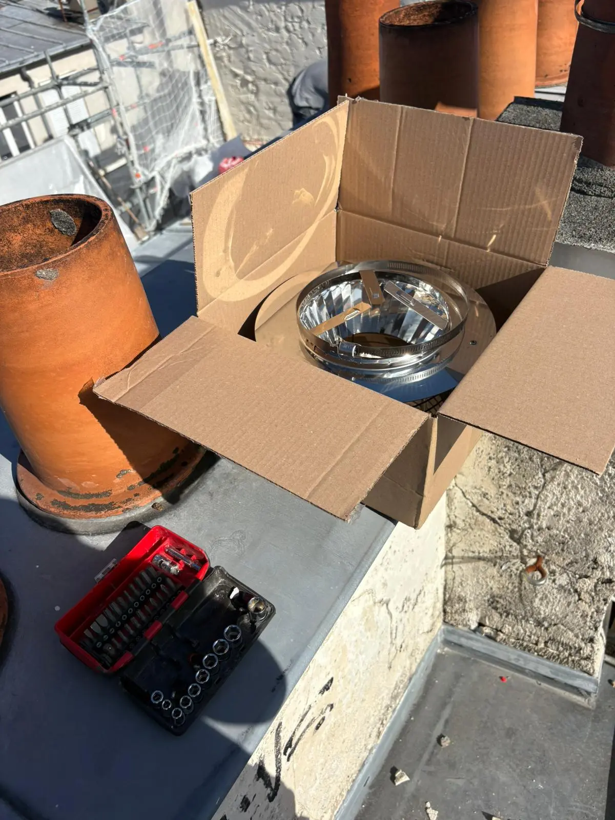 Chapeau de cheminée inox neuf sorti de son carton sur un toit, mitrons en terre cuite autour
