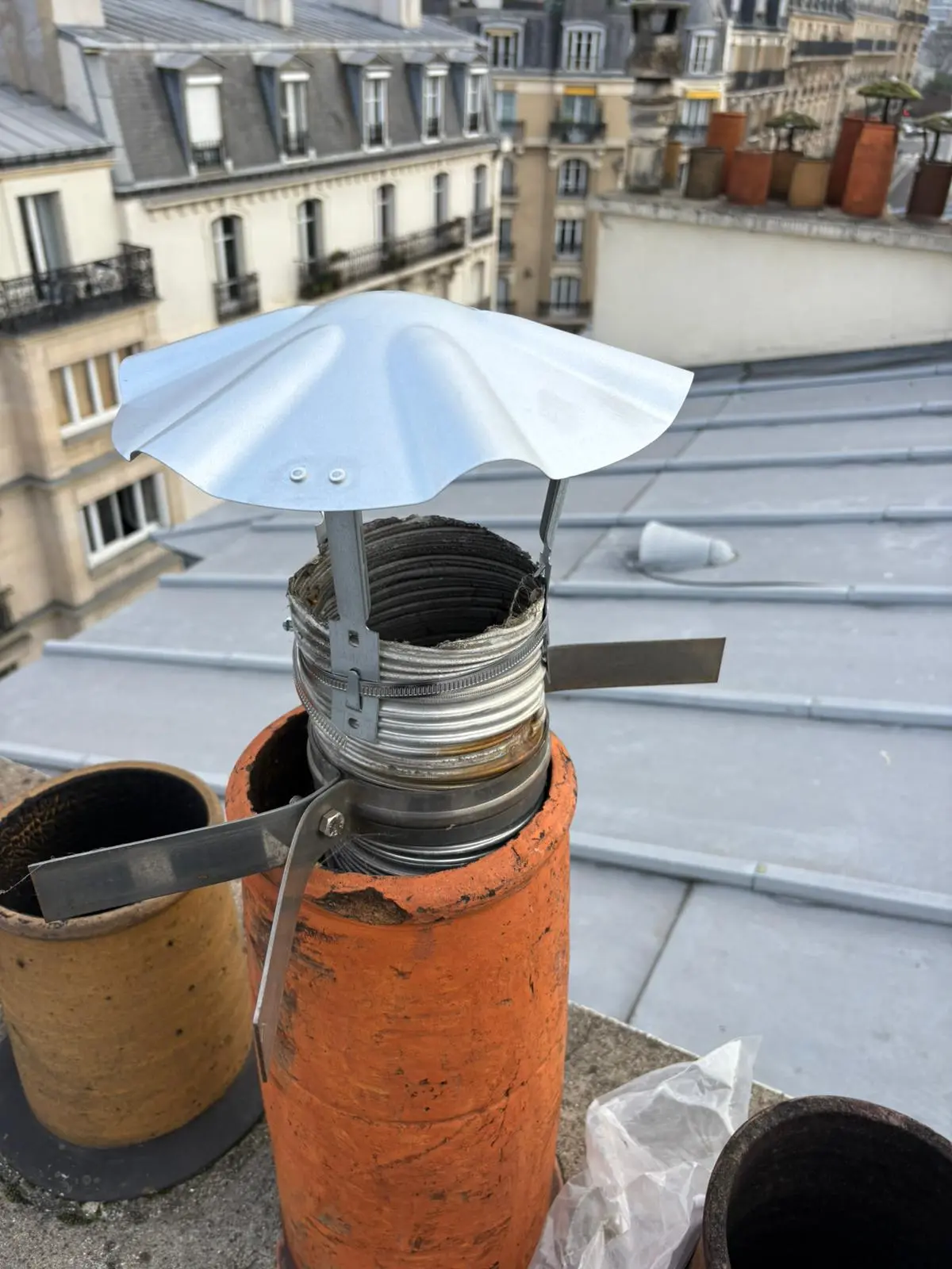 Chapeau galvanisé neuf fixé sur un tubage inox engagé dans un mitron en terre cuite, en toiture