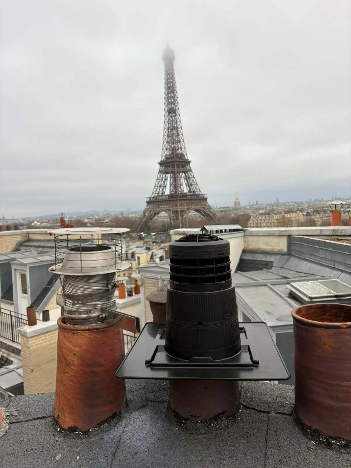 Deux sorties de tubage sur un toit parisien, chapeau neuf posé sur platine, tour Eiffel dans la brume