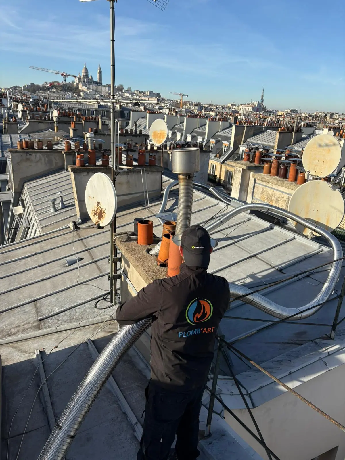 Technicien Plomb'Art engageant un tubage flexible dans une souche, Sacré-Cœur au loin sur la butte