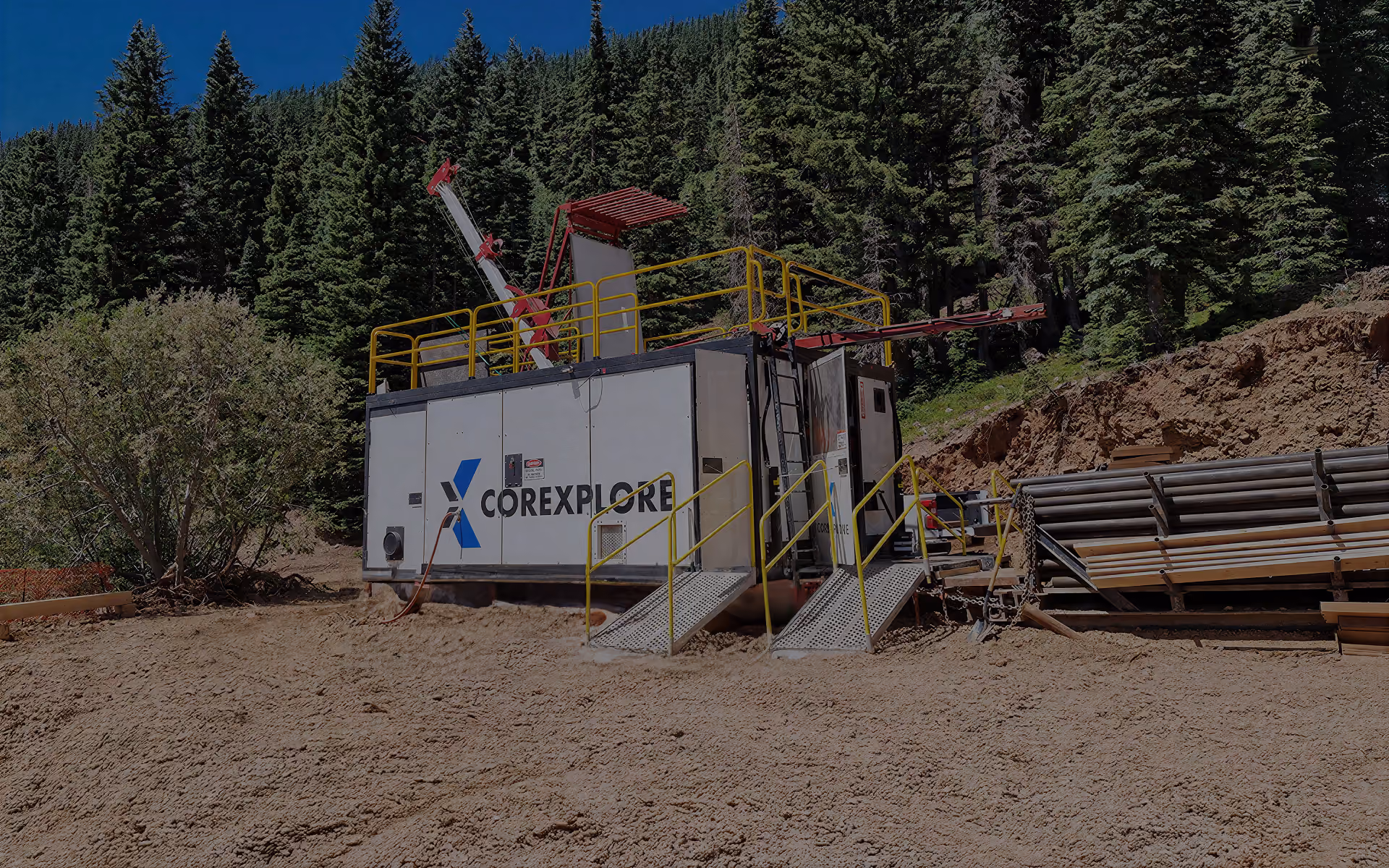 Corexplore drill shack and stacked drill rods at a forested hillside drill site