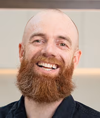 Headshot of Joe, a smiling bald man with a red beard