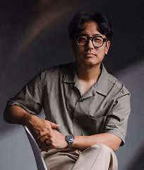 Portrait of Dan seated, wearing glasses and an olive short-sleeve shirt