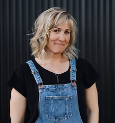 Headshot of Nancy in denim overalls against a dark panelled wall