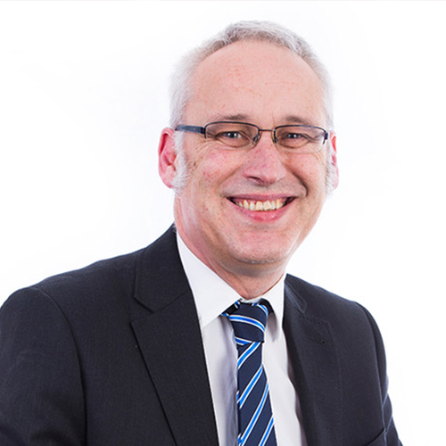 Smiling middle-aged man wearing glasses, suit, white shirt, and striped blue tie on white background.