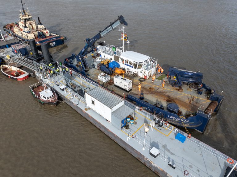 Aerial view of a working barge alongside a tugboat and smaller boats on brown water.