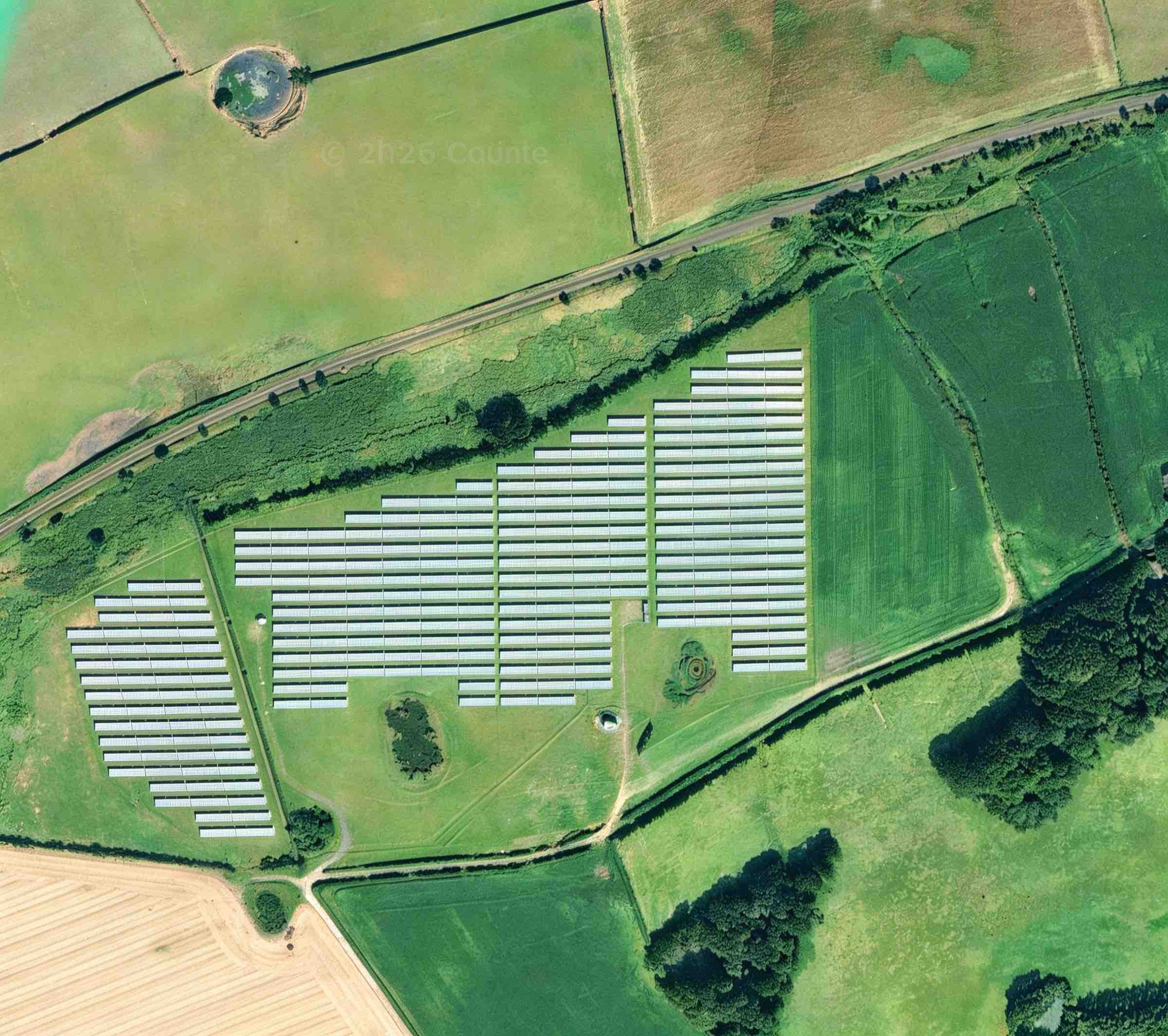 Aerial view of solar panels arranged in rows within green fields and farmland.