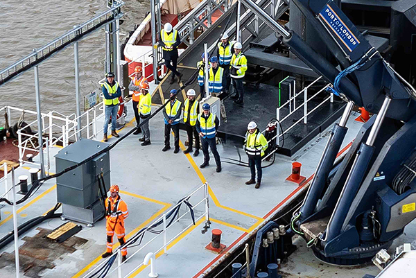 Workers in safety gear standing on a ship deck near heavy lifting equipment