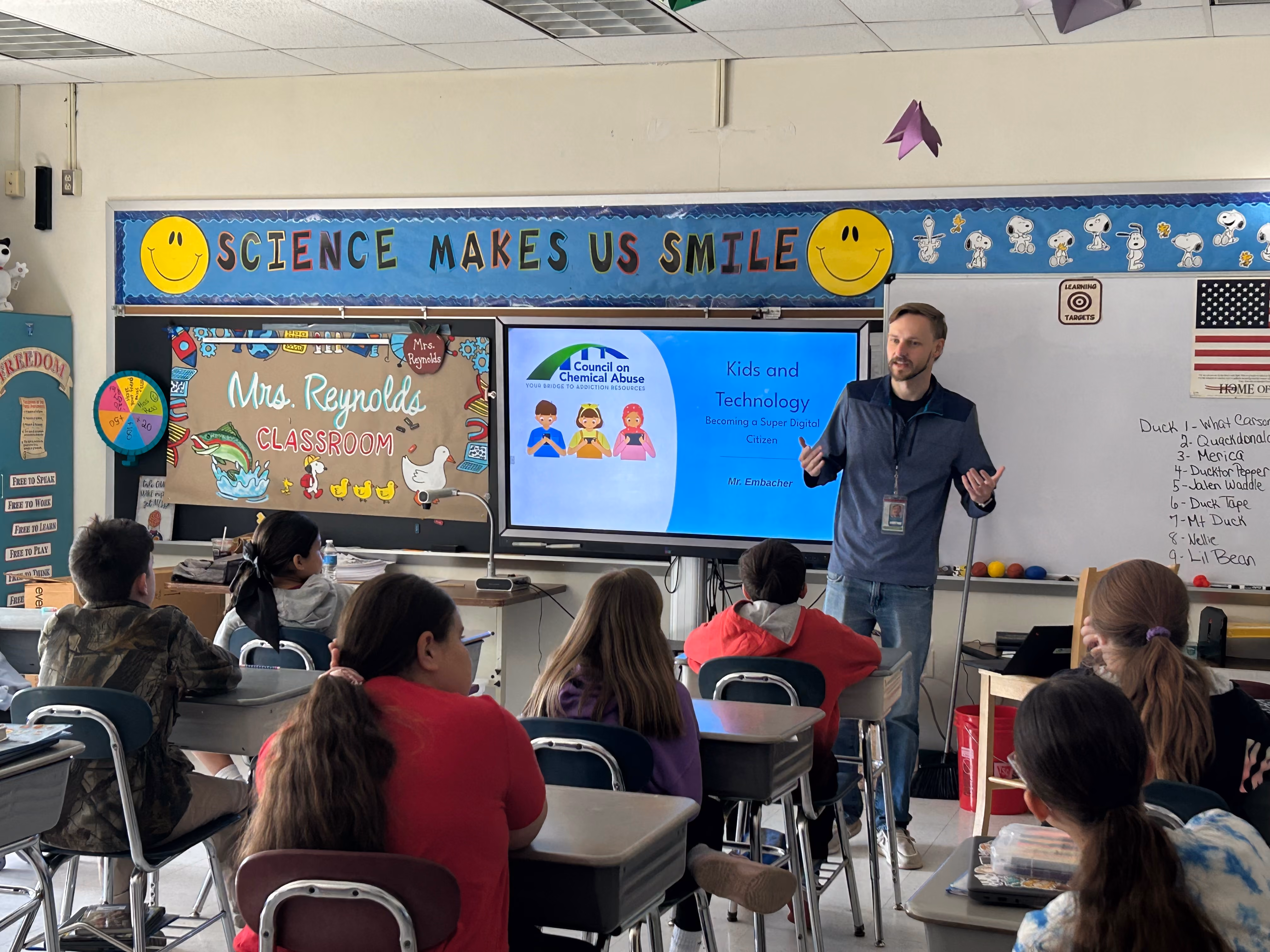 Teacher presents digital citizenship lesson to attentive elementary students in a colorful classroom setting.