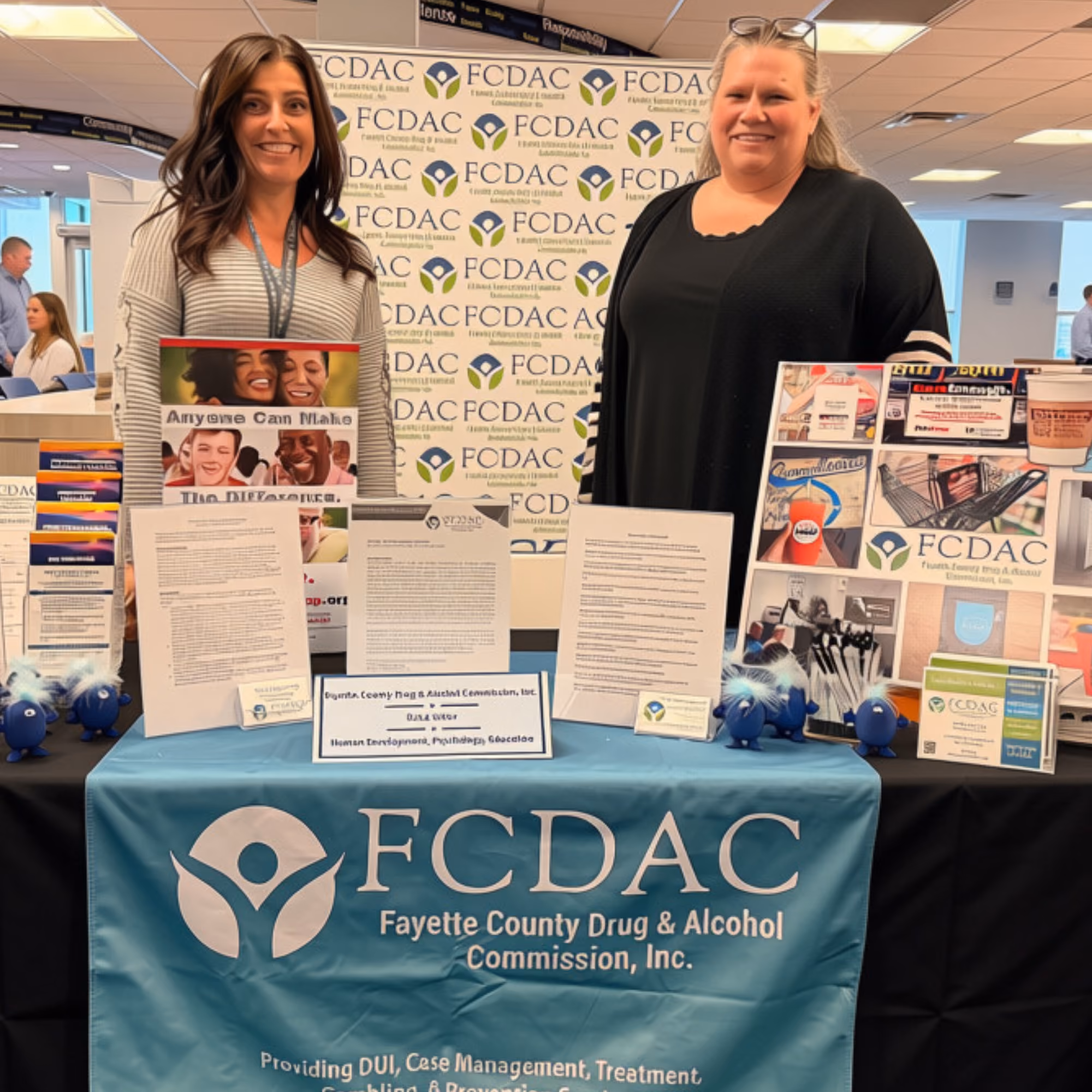 Two women standing behind Fayette County Drug & Alcohol Commission display booth with brochures and visuals.