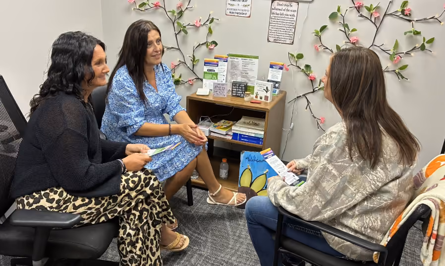 Three women sitting and talking in an office decorated with pink flowered vines on the wall.