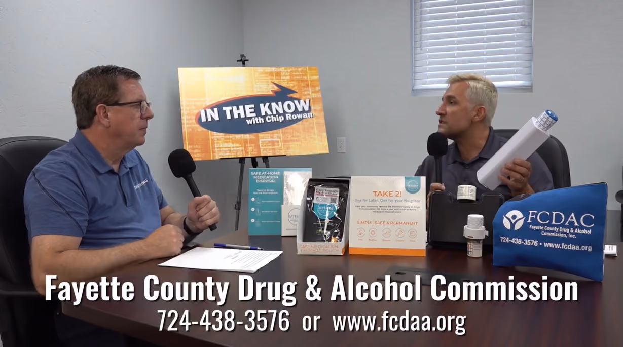 Two men holding microphones at a table with Fayette County Drug & Alcohol Commission materials.
