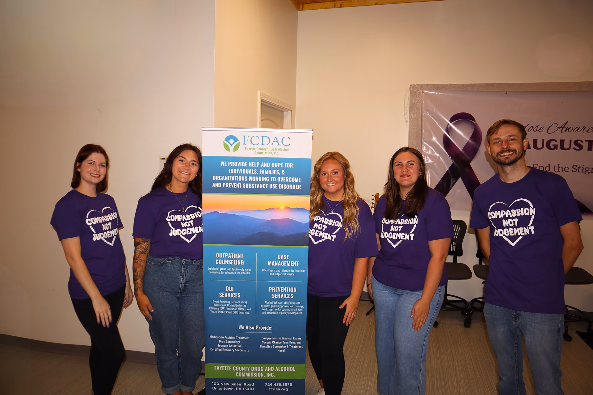 Five people wearing purple 'Compassion Not Judgement' shirts stand beside a Fayette County Drug and Alcohol banner.