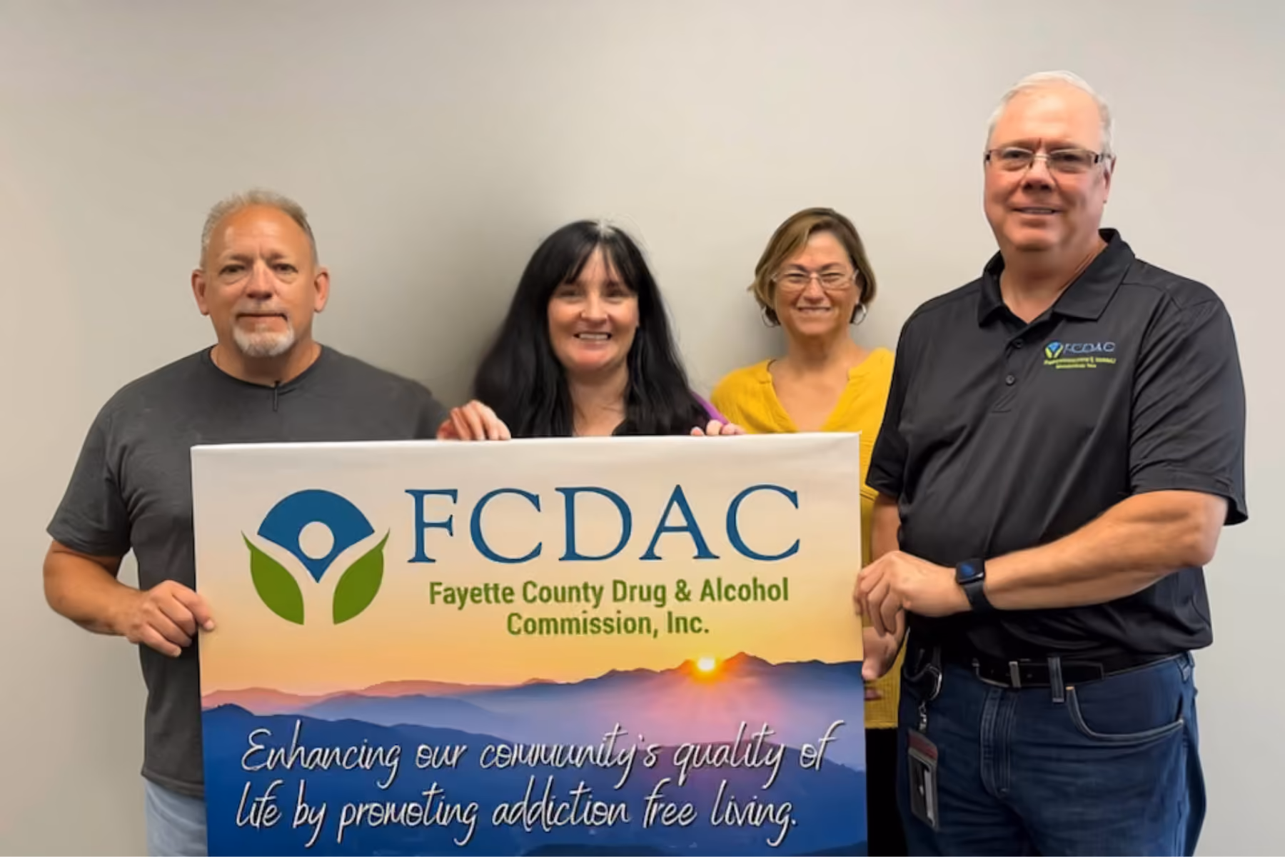 Four people holding a Fayette County Drug & Alcohol Commission sign with a sunset and mountains background.
