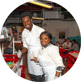 A man and woman are standing in a kitchen with a red table.