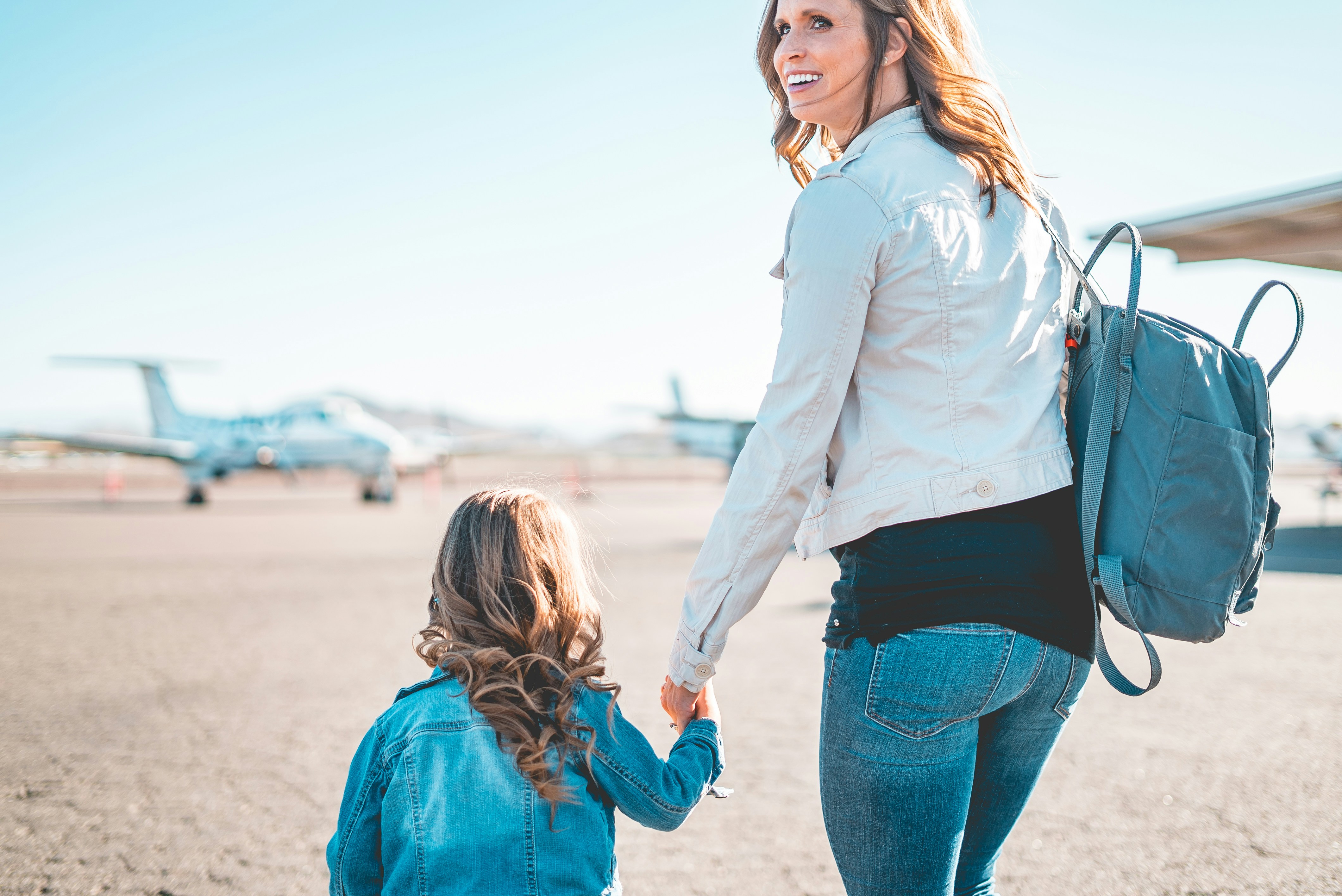 Mother and daughter walking hand in hand across the tarmac with private jets in the background