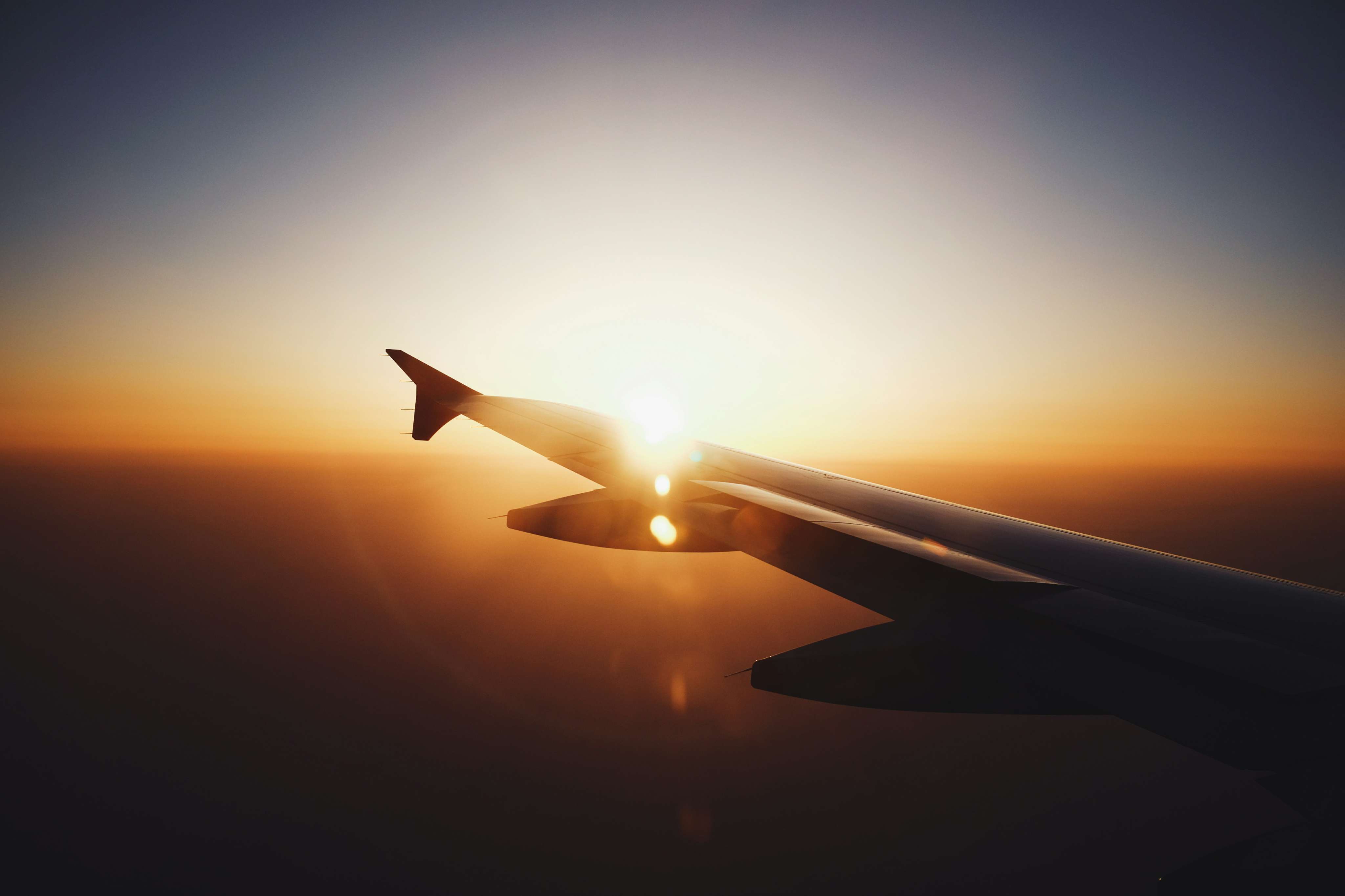 Airplane wing silhouetted against a sunset