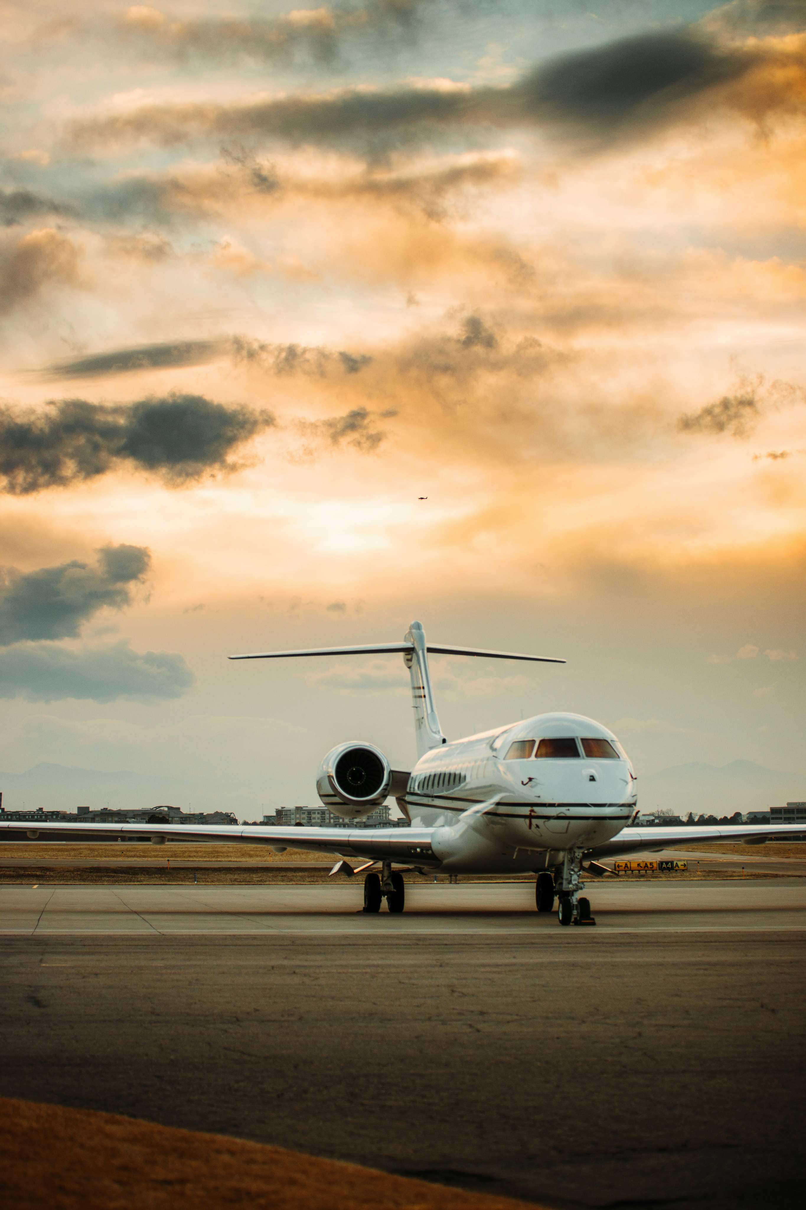 White private jet parked on runway under a cloudy sunset sky.