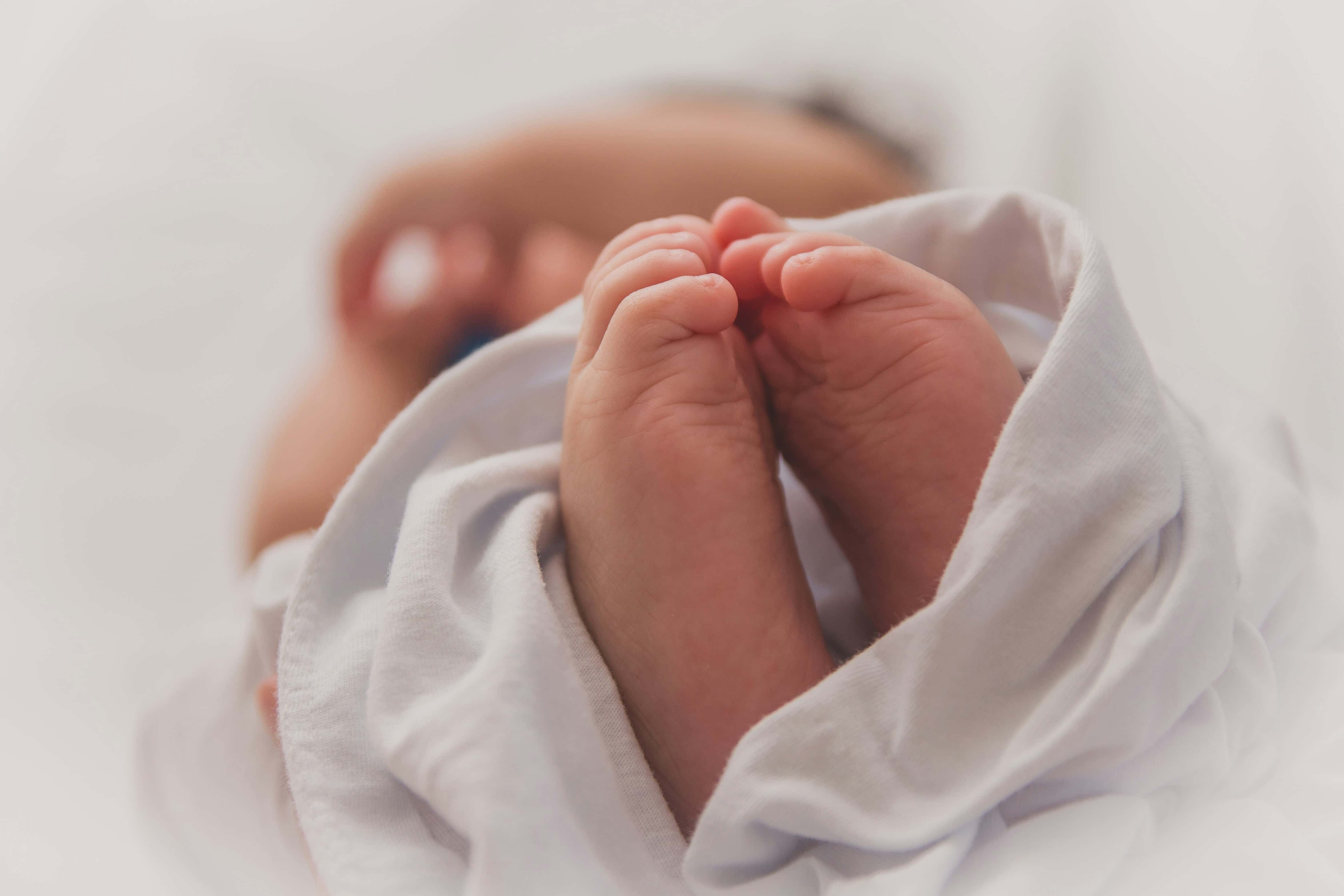 Close-up of a newborn baby's hands wrapped in a white blanket, resting near a parent's chest.