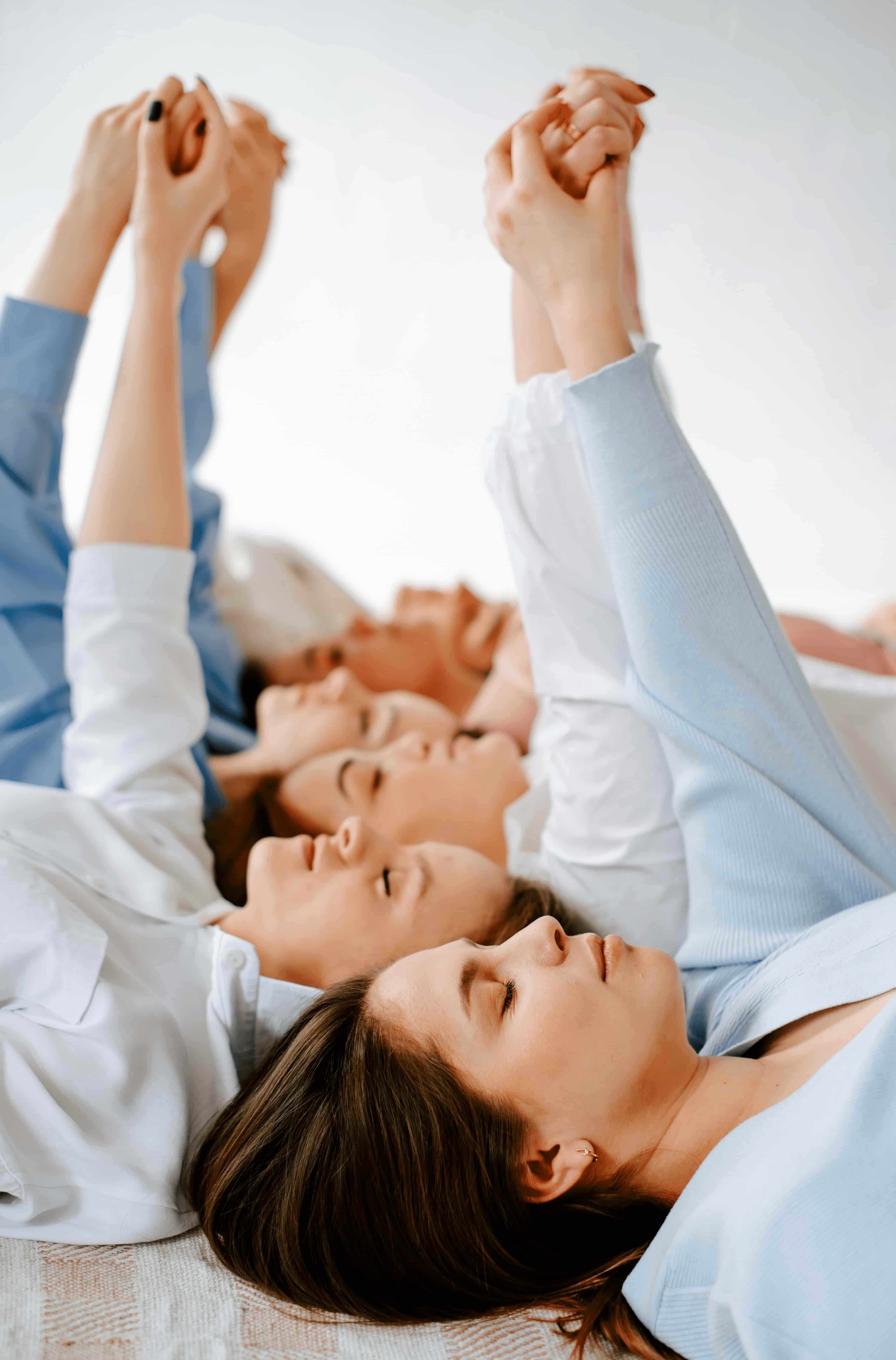 Women lying down with their heads together and hands clasped overhead, eyes closed, smiling.
