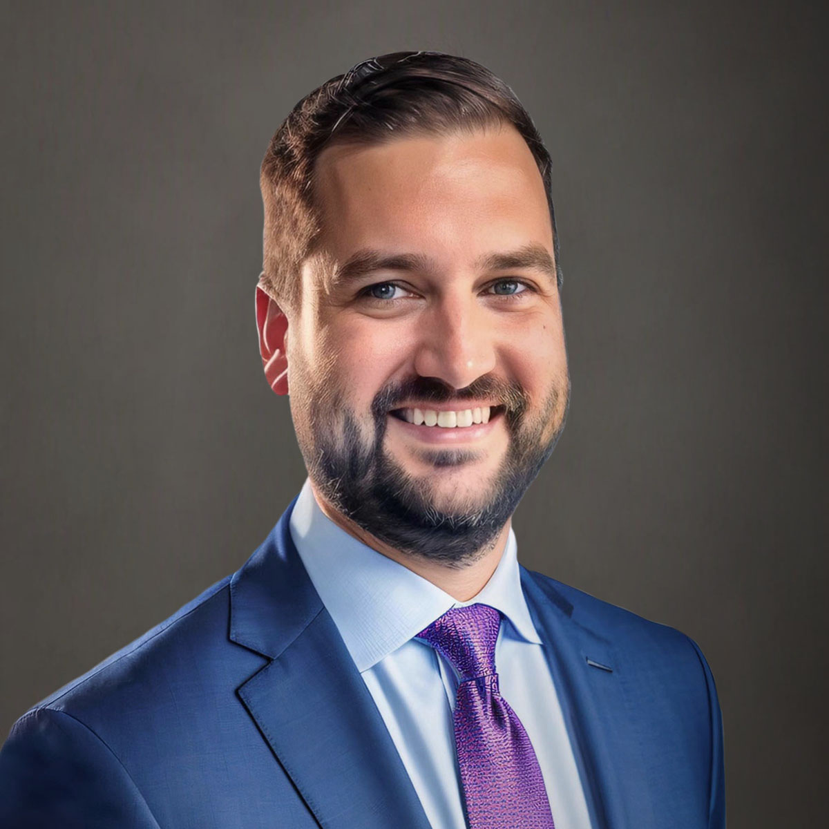 Man smiling with a blue suit and purple tie with a gray backdrop