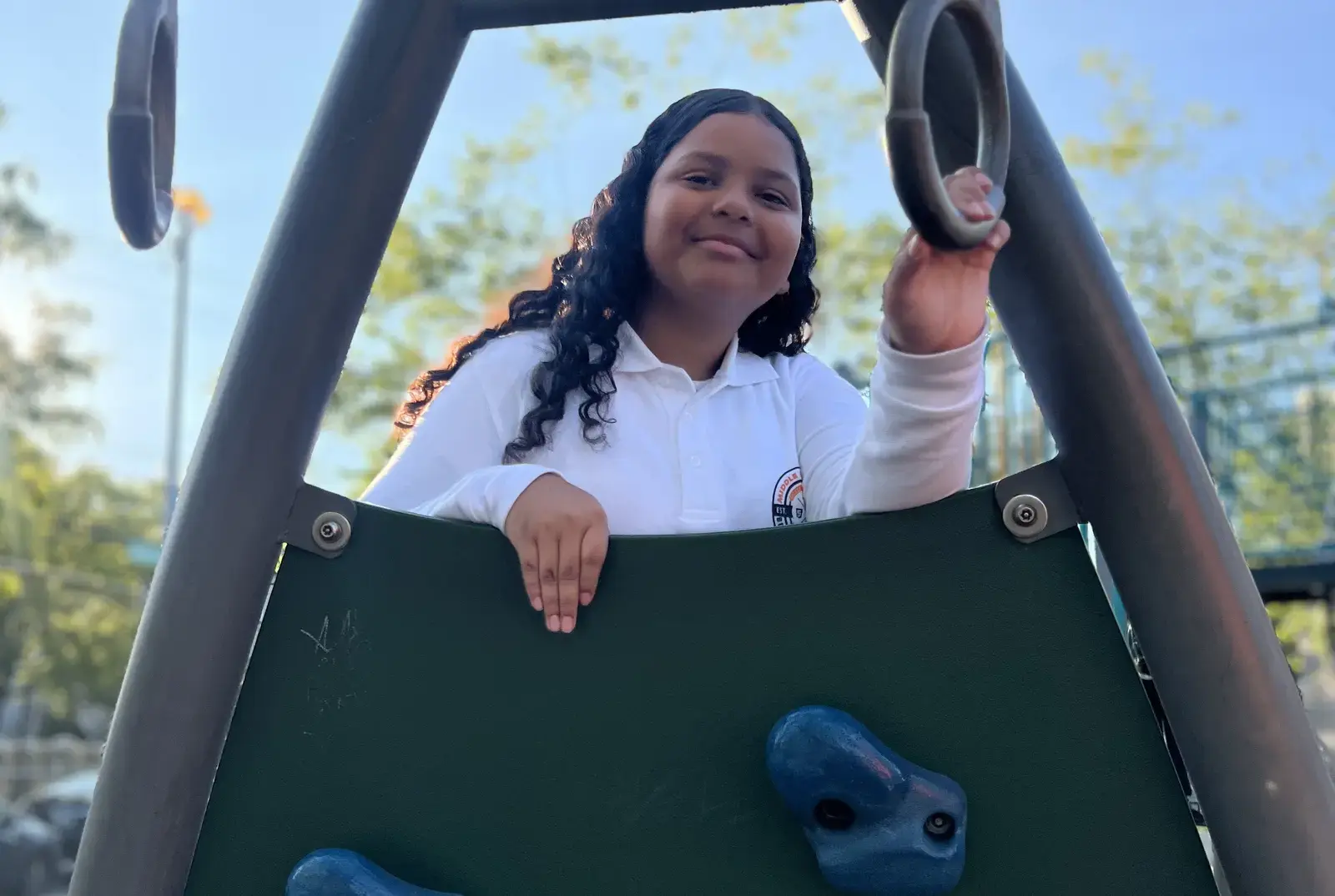 Smiling student in uniform climbing playground equipment outdoors