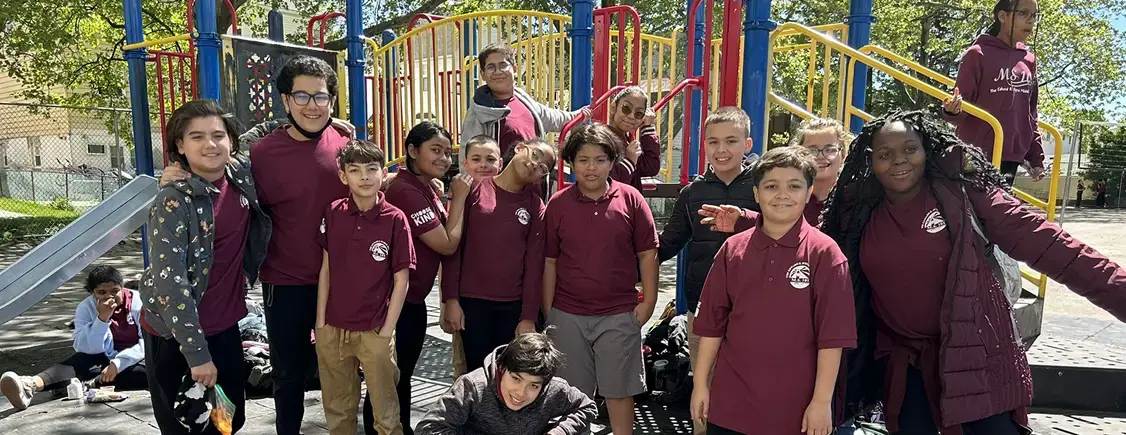 Students in maroon school uniforms posing together on playground