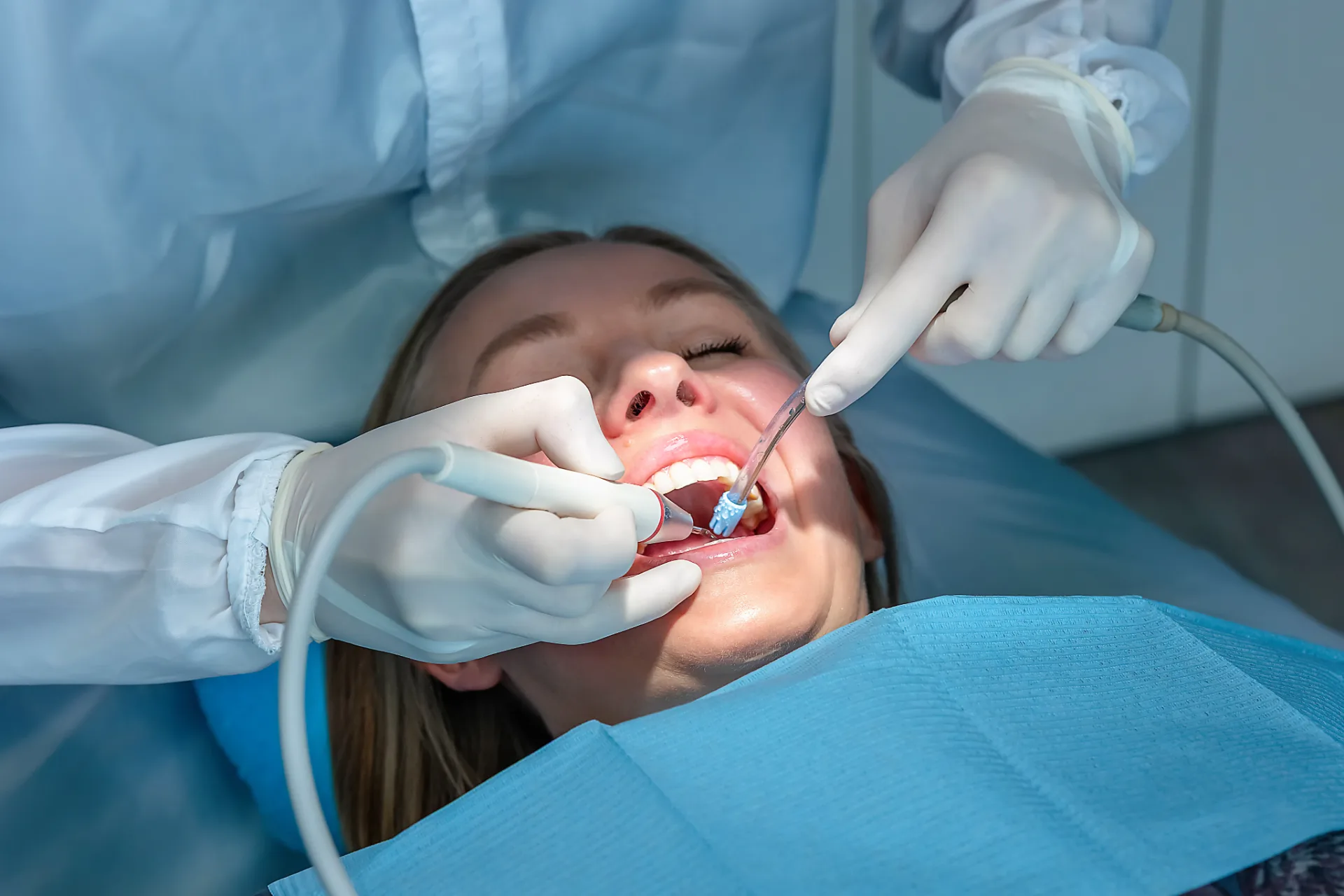 Dentist wearing gloves using dental tools to treat a woman reclining in a dental chair.