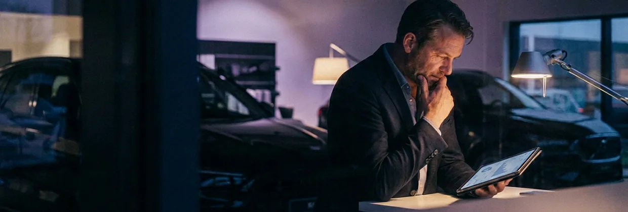 A man sitting in a car dealership, analysing some data on a tablet.