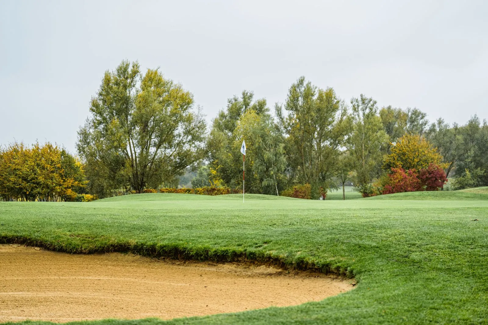 Sandbunker vor einem Grün mit Fahne am Golfpark am Löwenhof, im Hintergrund herbstlich gefärbte Bäume