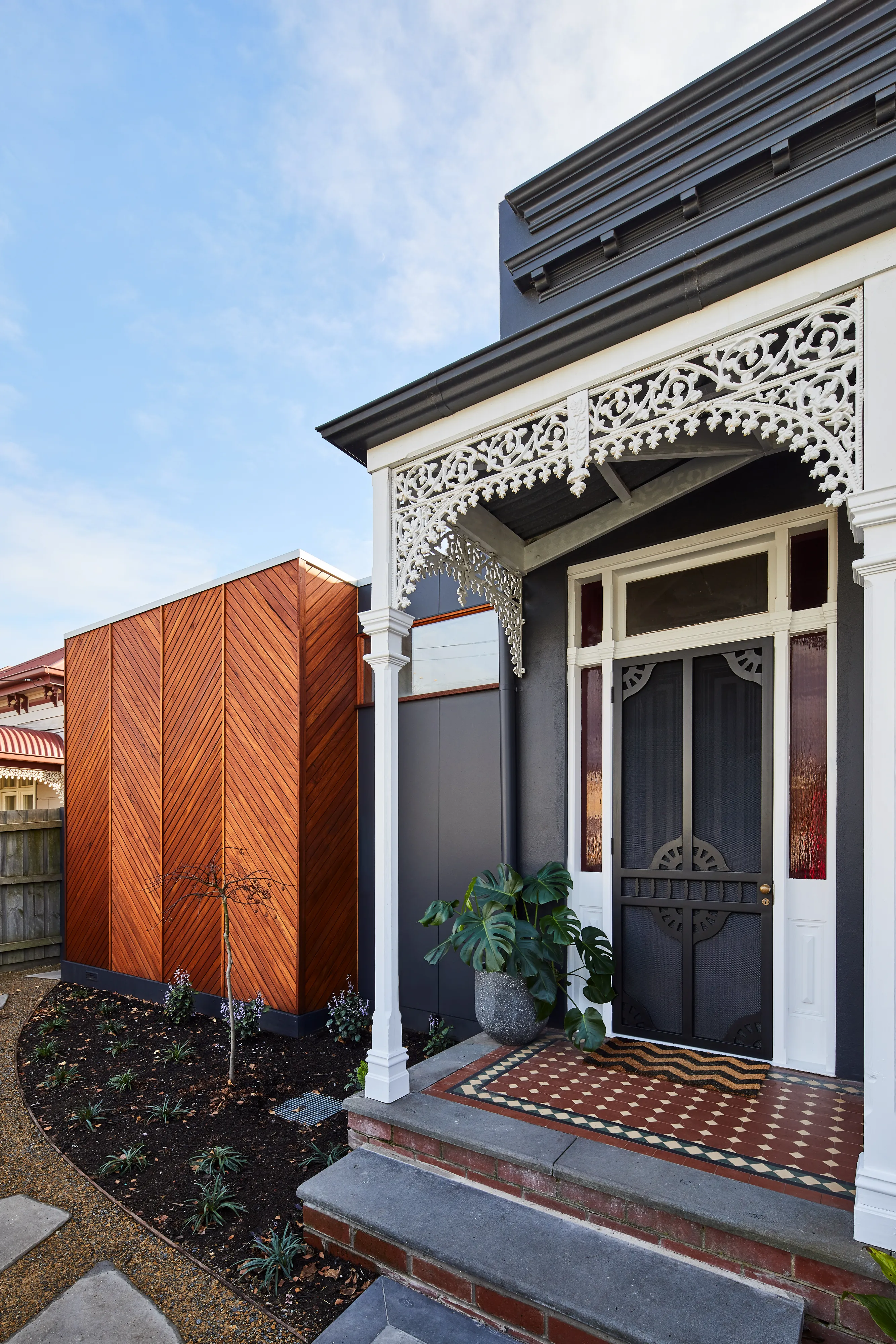 Front porch of a house with decorative white trim, black door, tiled floor, and plant in a pot.