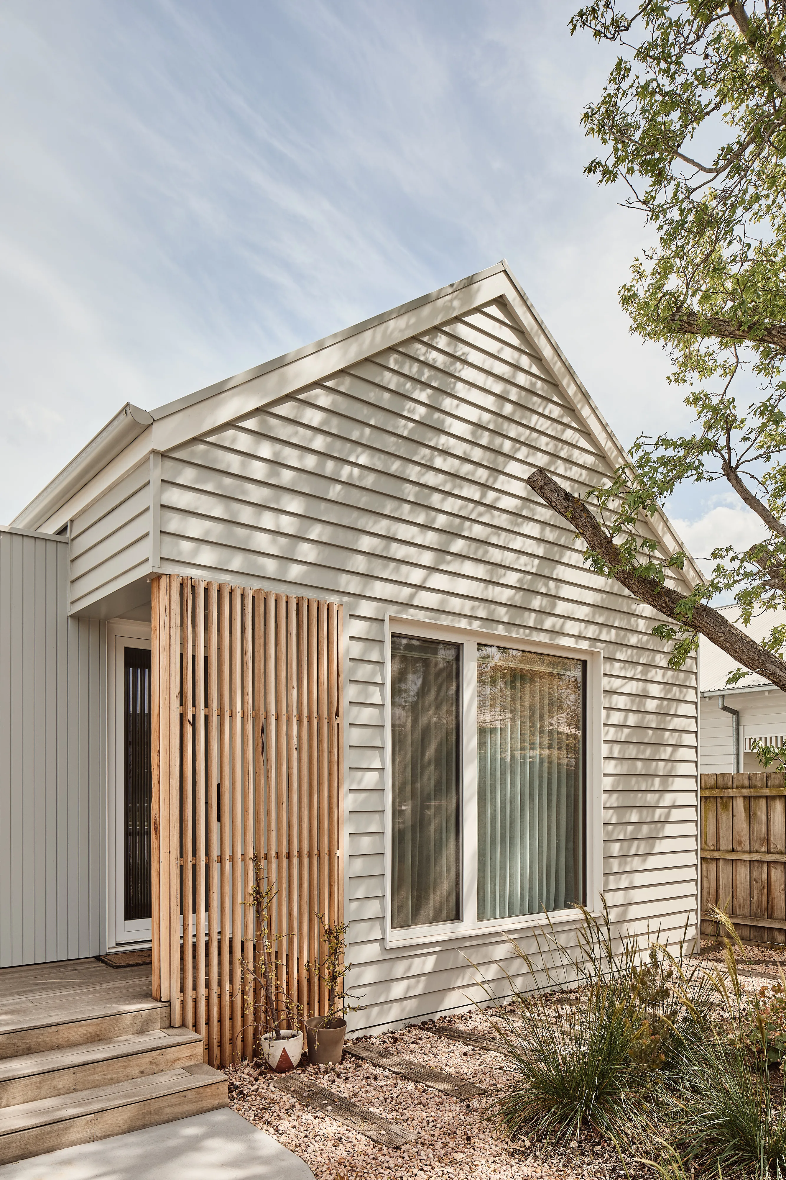 Modern white house exterior with vertical wooden slats by the entrance and gravel garden with plants.