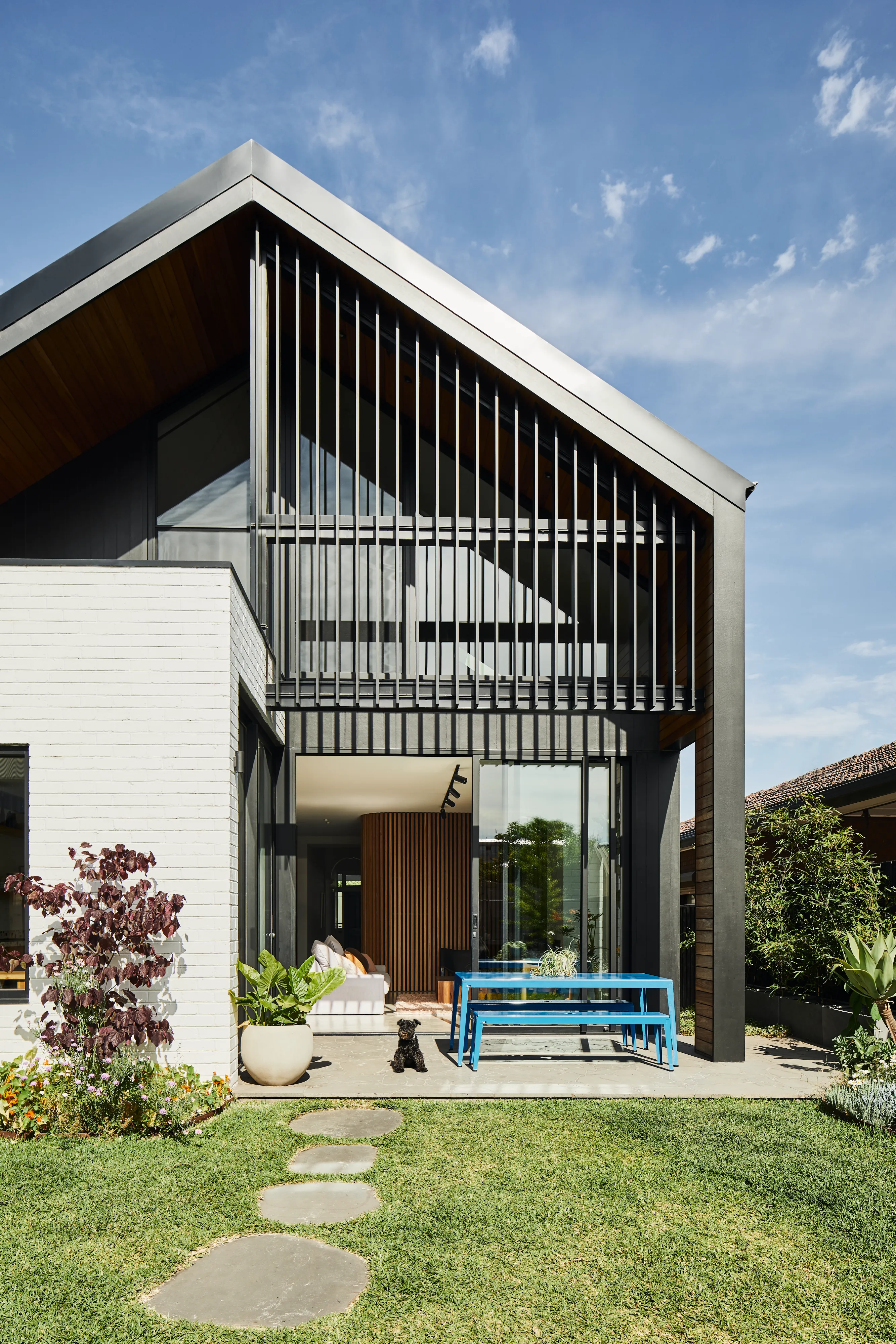 Modern home with black metal vertical slats, blue outdoor table, and a small black dog on the patio.