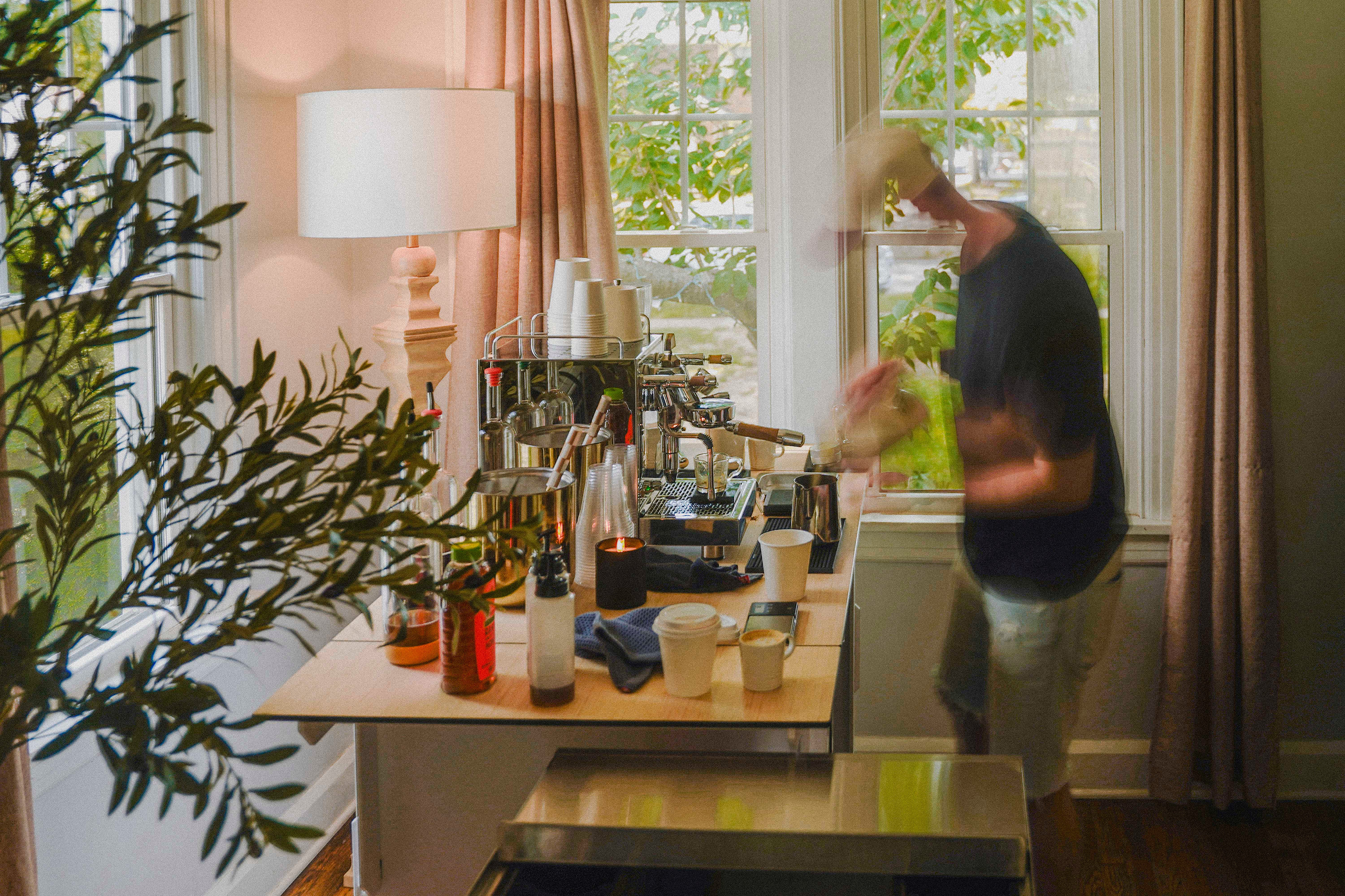 Barista preparing coffee espresso machine on a wooden table near a window.