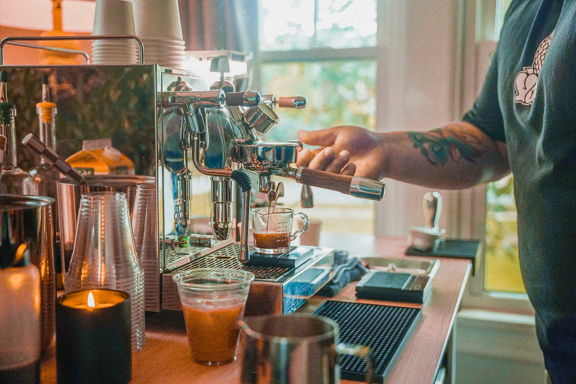 Barista with tattooed arm making espresso with a professional machine and glass cup on the tray.