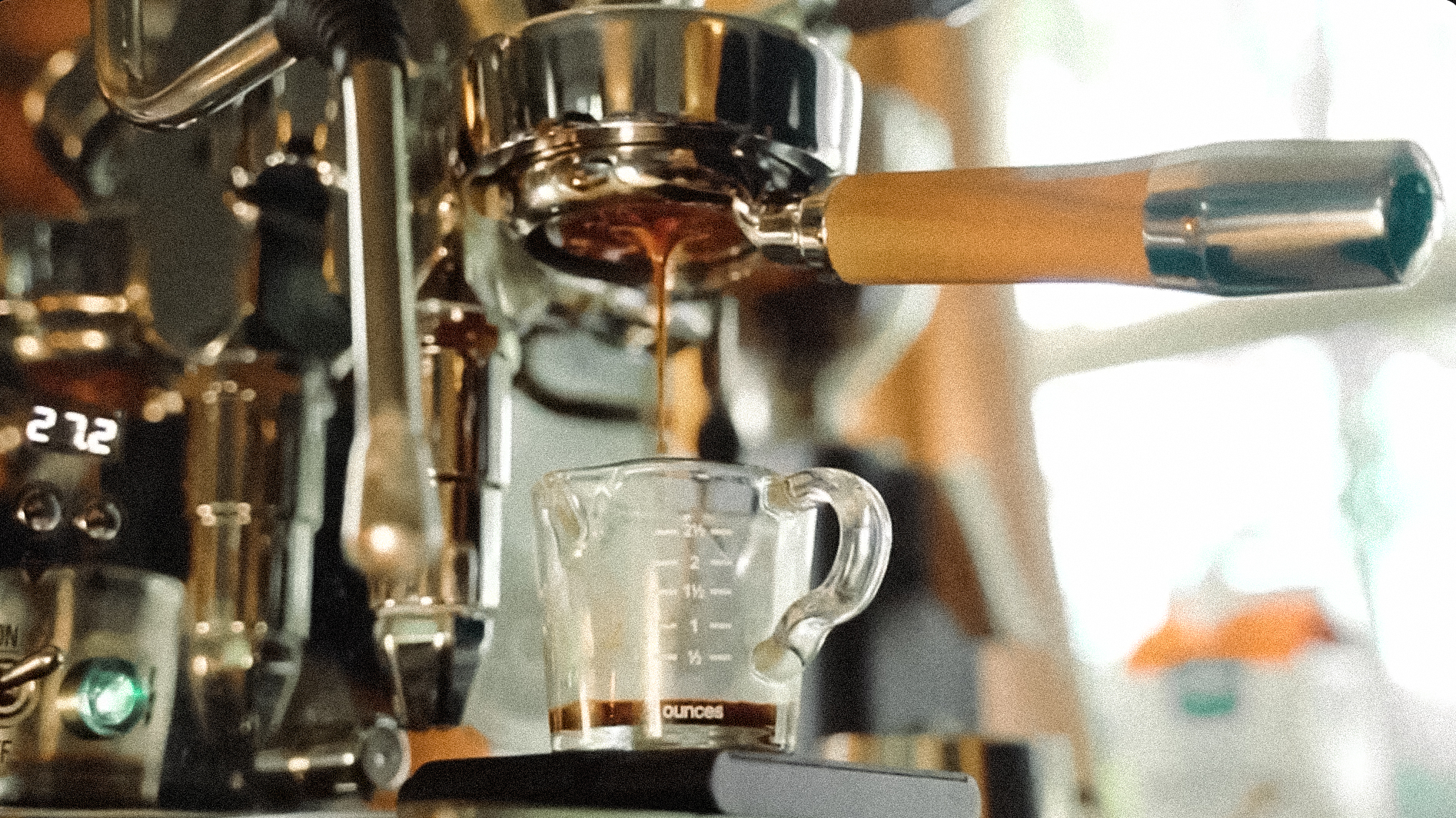Espresso dripping from a portafilter into a glass measuring cup on a scale.
