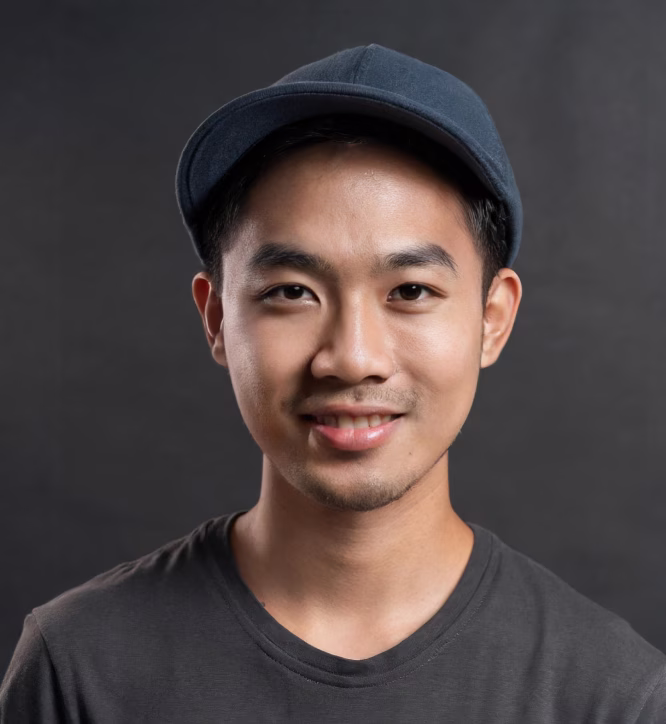 Young man wearing a navy blue cap and dark gray t-shirt smiling against a dark background.
