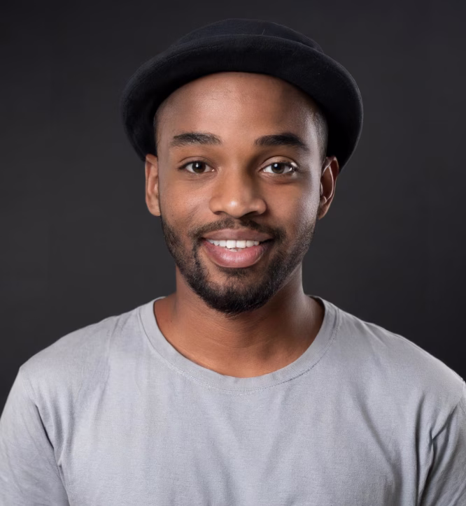 Smiling young man wearing a black hat and light gray t-shirt against a dark background.