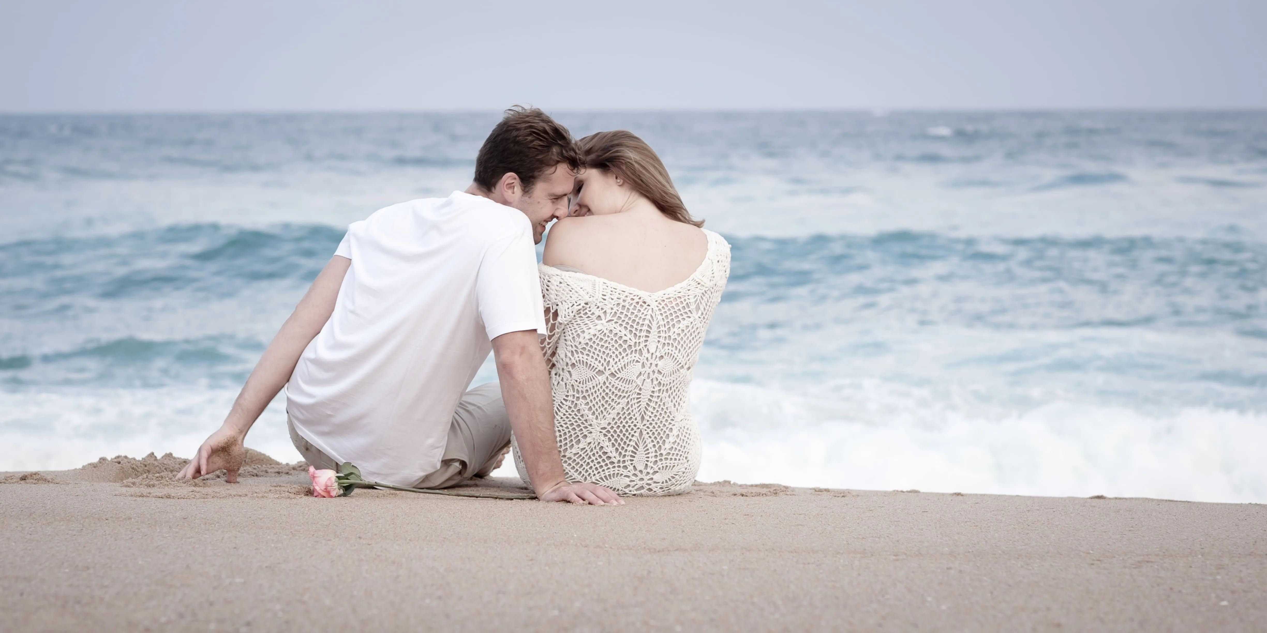 Couple sitting closely together by the ocean.