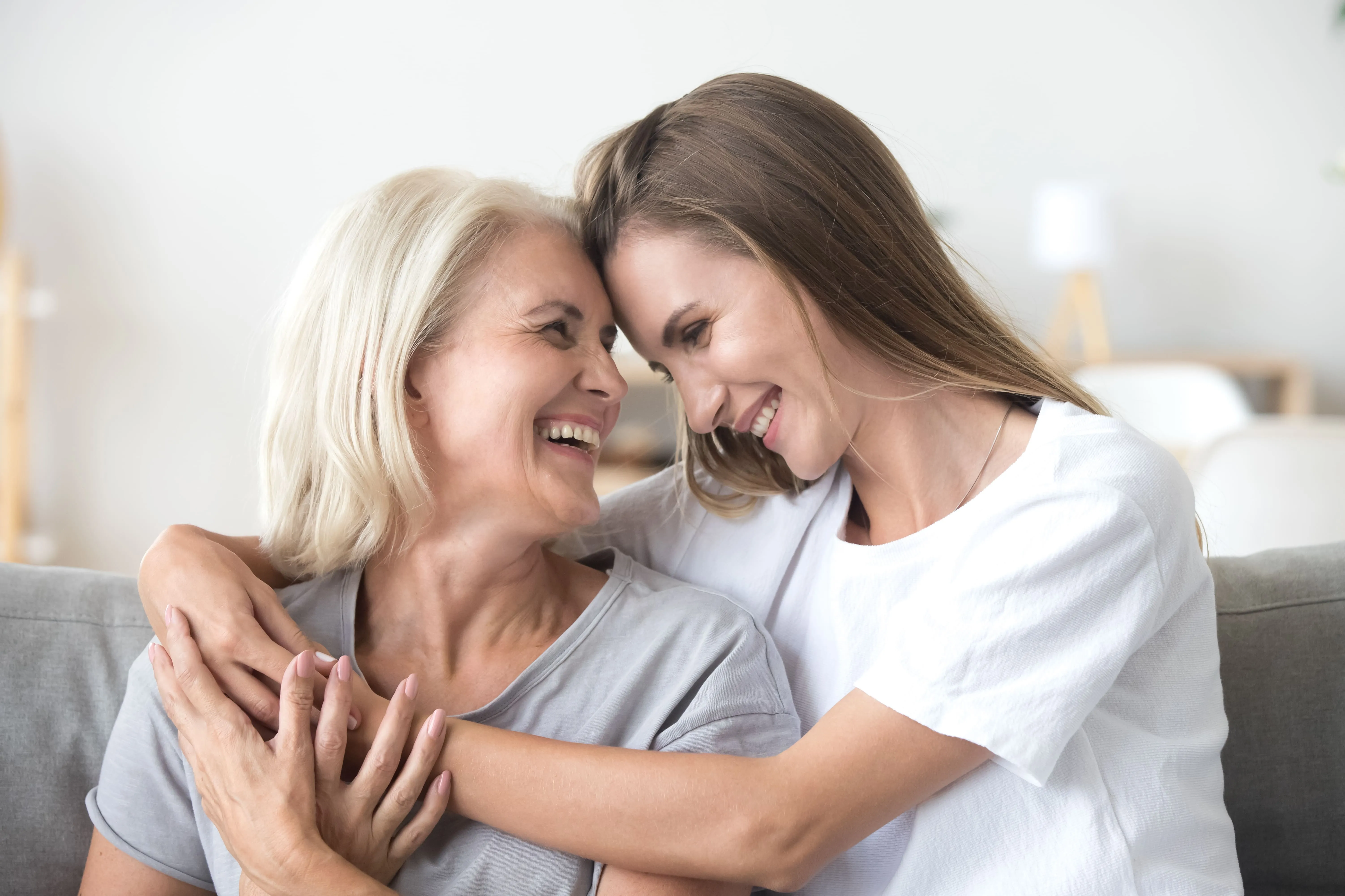 Adult daughter and mother embracing and smiling together.