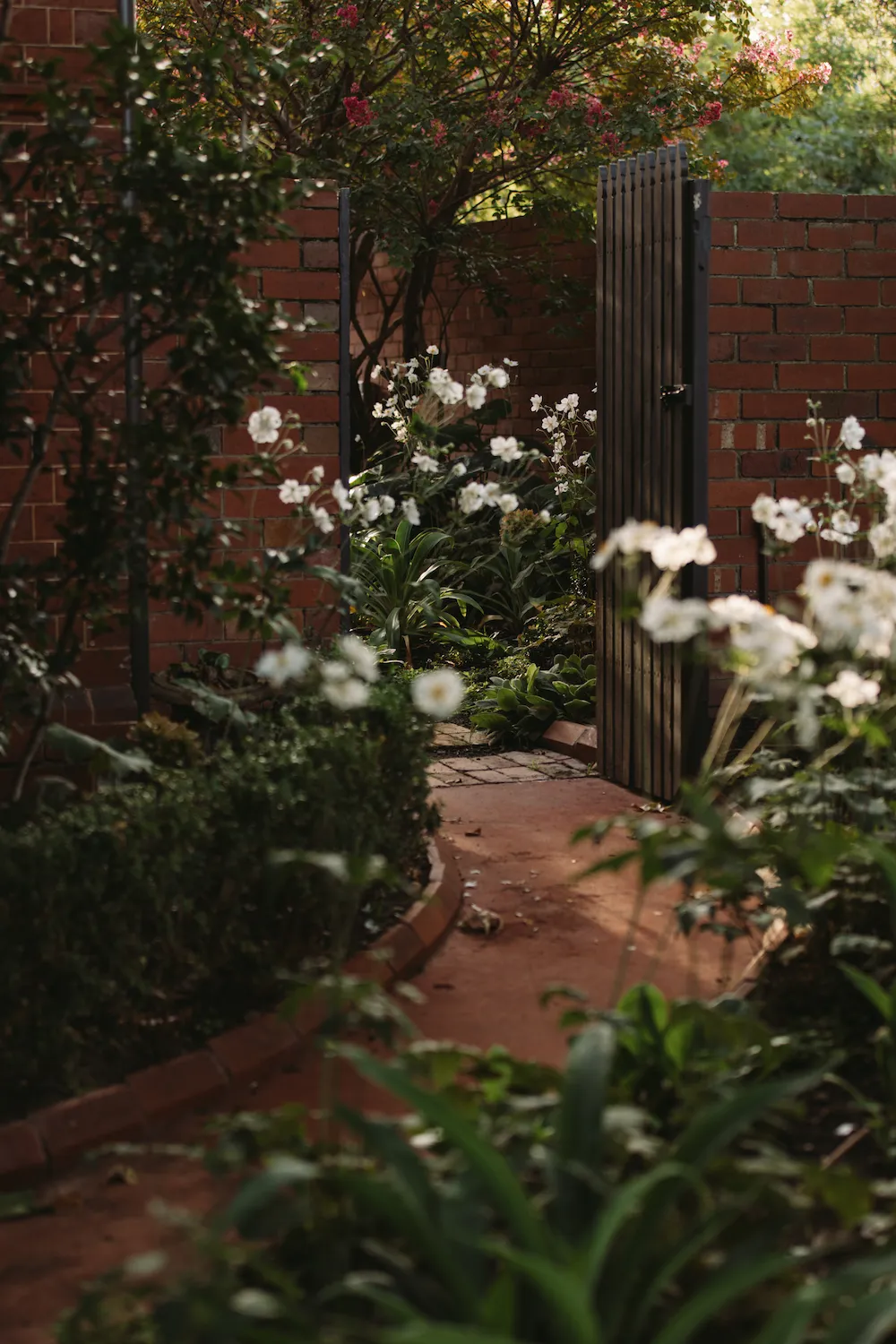 A red brick flower lined path winding through a gate