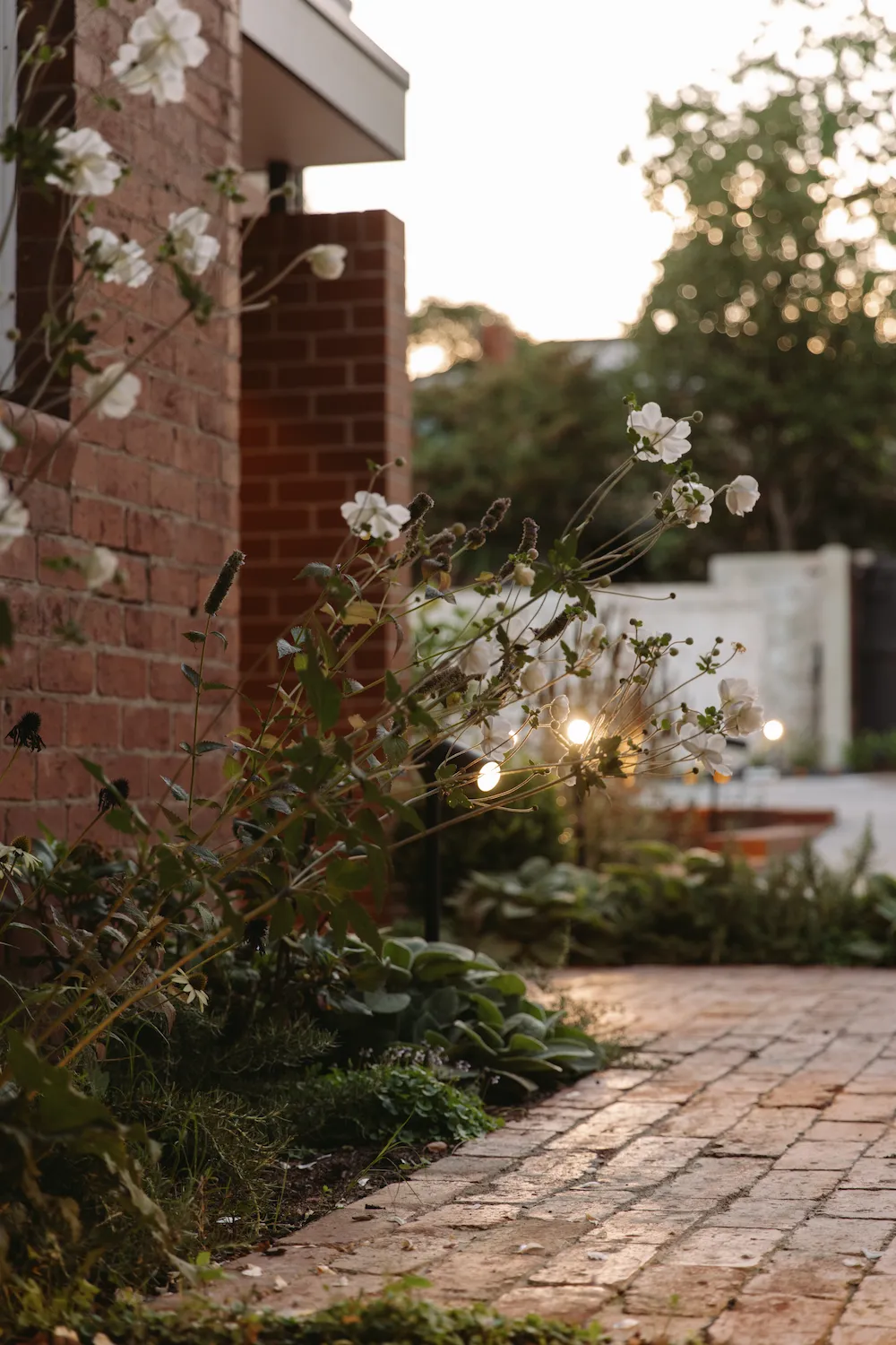 A red brick pathway lined with flowers down the side of a house