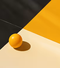 Orange placed at the intersection of yellow, cream, and dark surfaces creating geometric contrast and shadow.